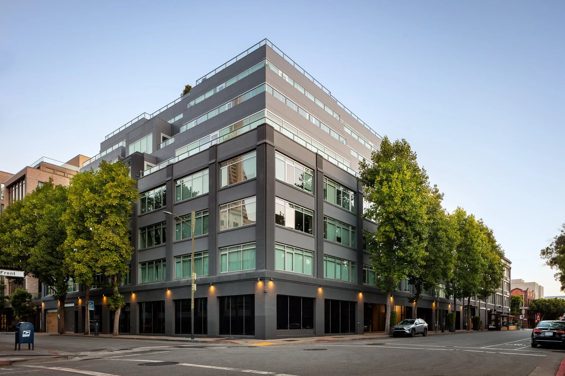 Modern multi-story building on a city corner with trees and cars, street signs, clear sky