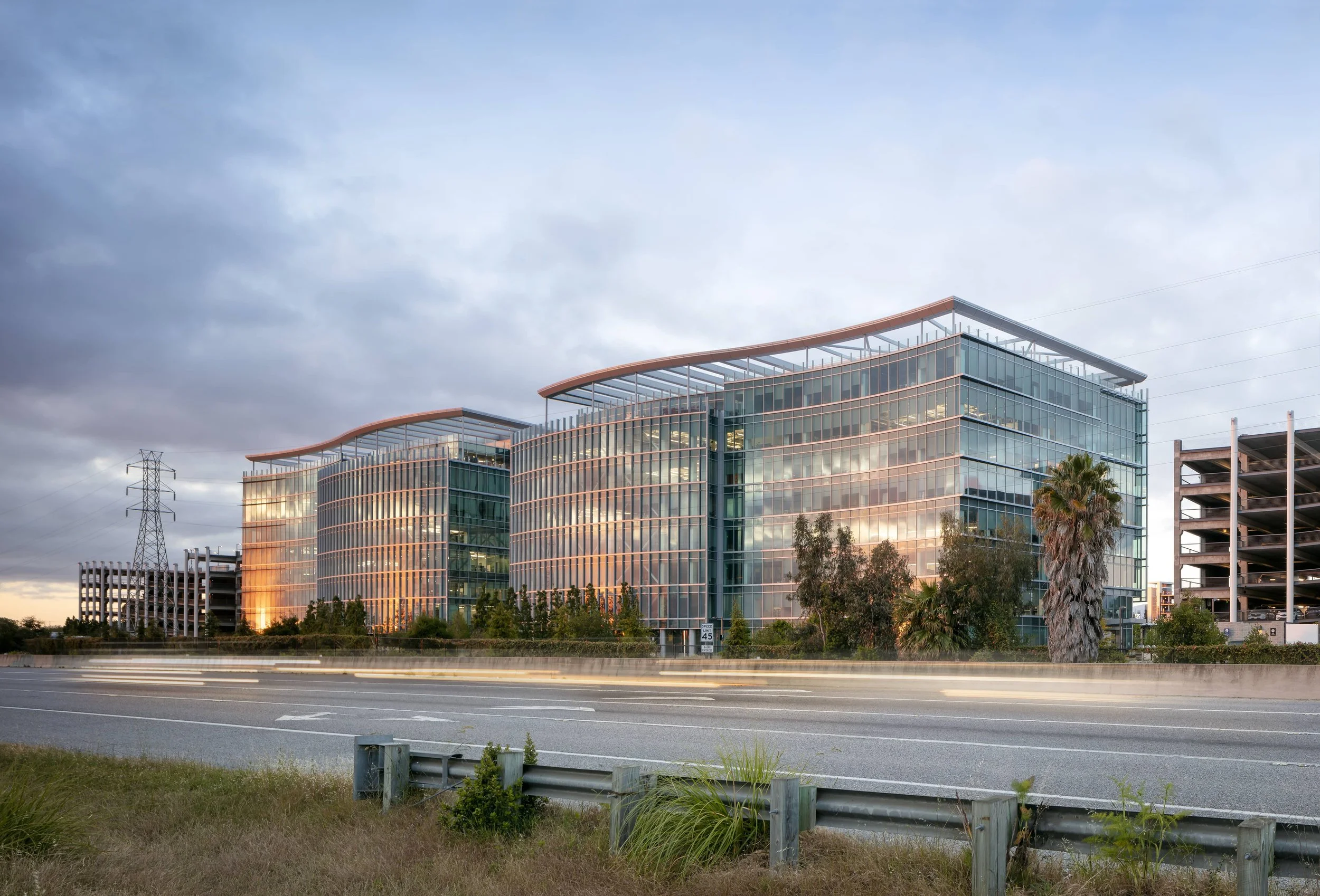 Modern glass office building reflecting the sunset sky with blooming palm trees in front.