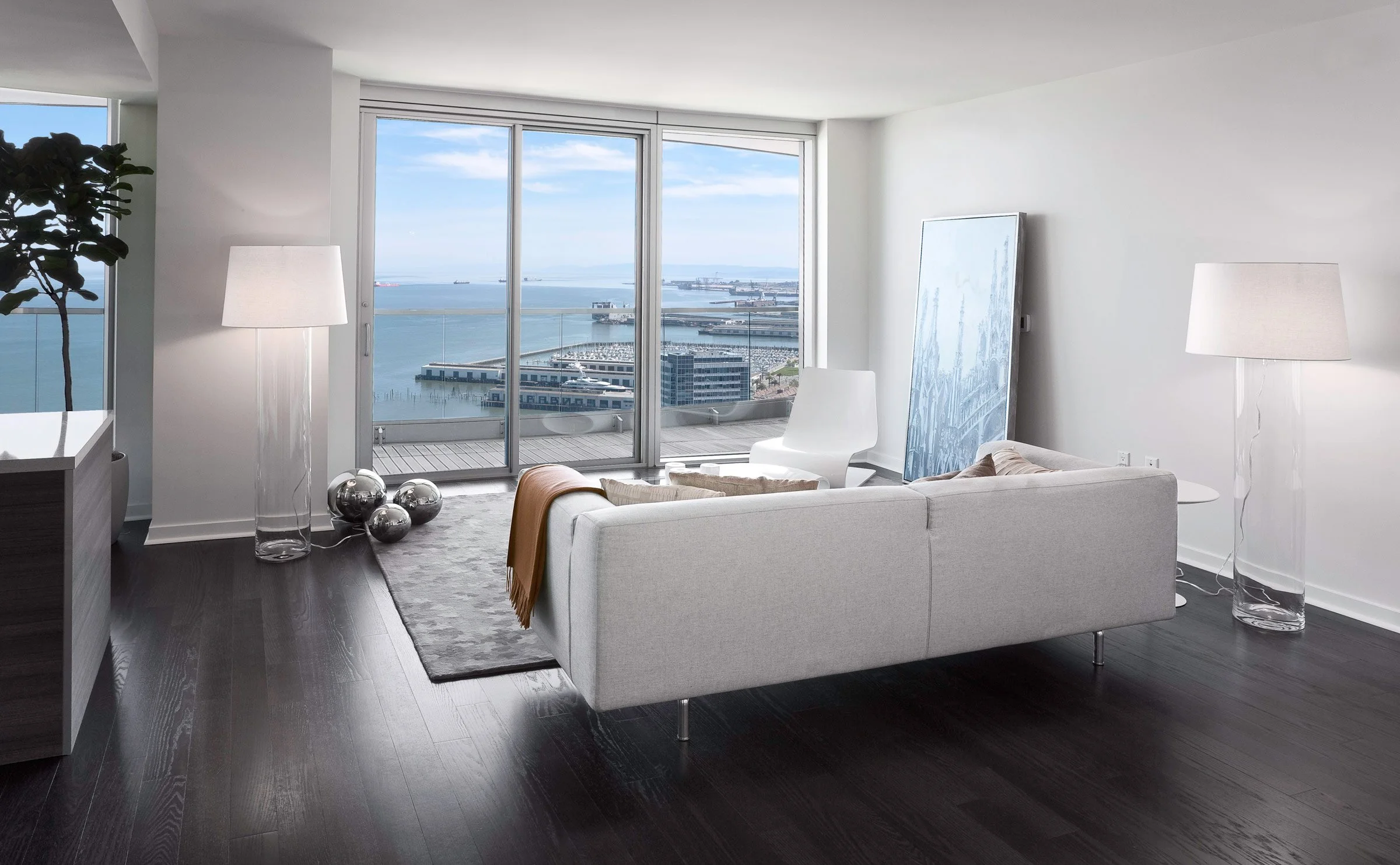 Modern living room with a white sofa facing large windows with a view of a harbor and blue sky.