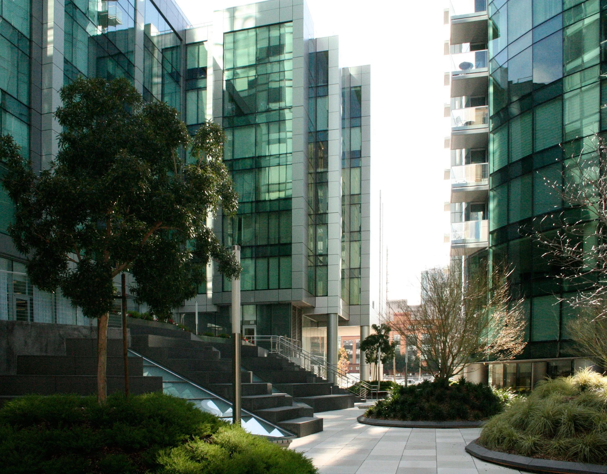 Modern office building courtyard with trees, plants, stairs, and glass facades.