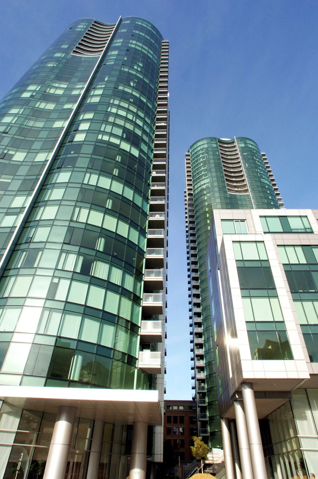 Two modern glass high-rise buildings with rounded design and balconies, under a clear blue sky.