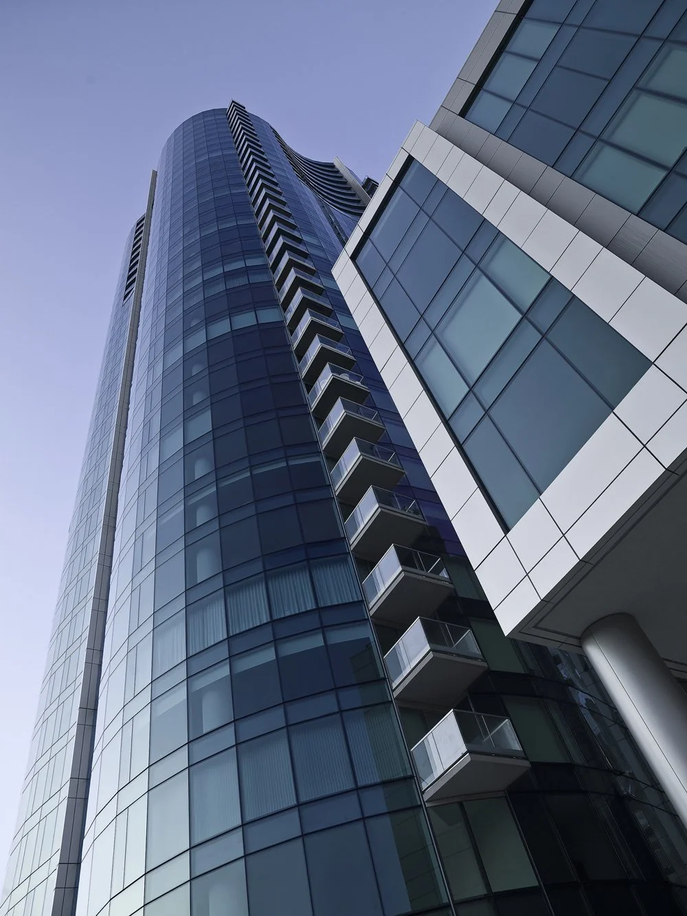 Looking up at a modern glass skyscraper with reflective windows and balconies.