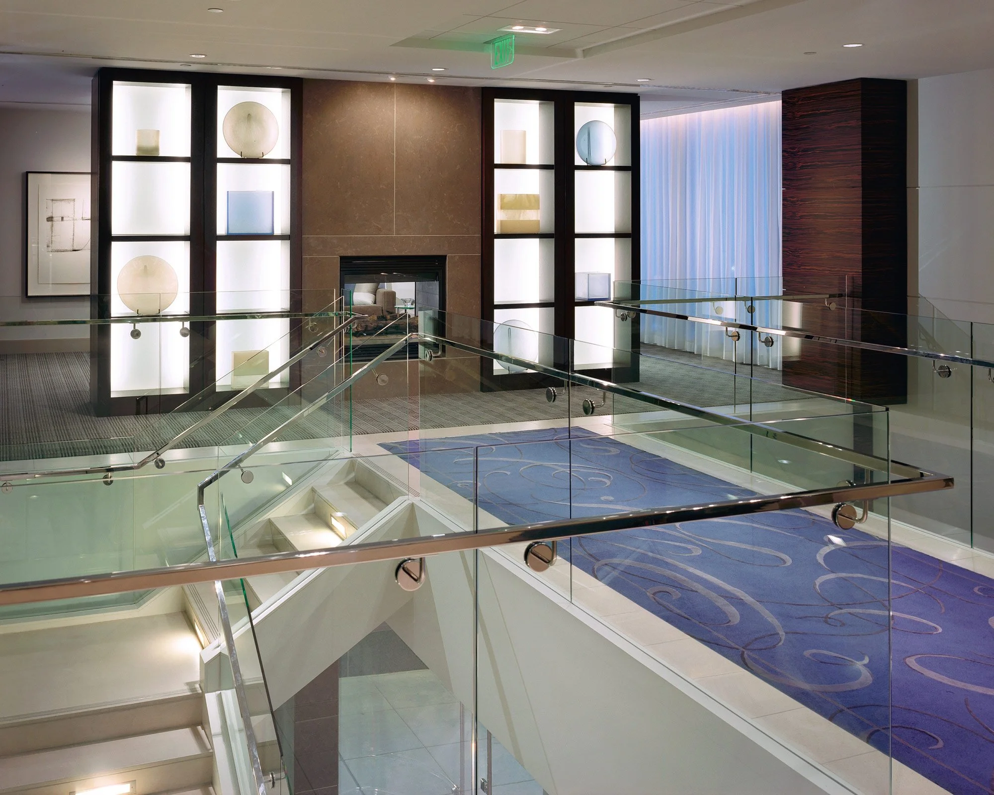 Interior of a modern building with glass railings, a blue patterned carpet, a fireplace, and decorative wall displays.