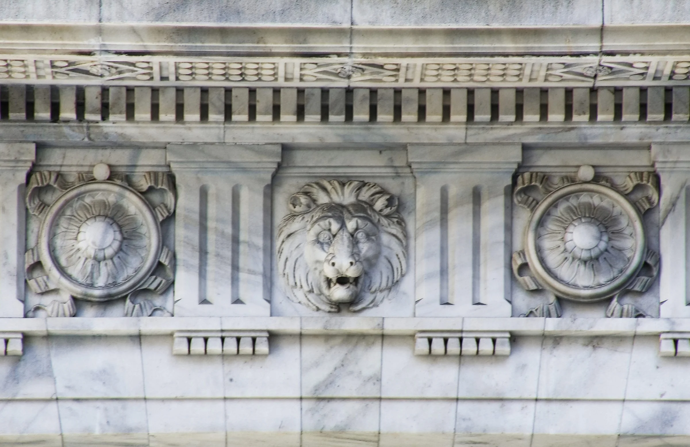 Marble architectural detail with a lion's head sculpture in the center and decorative circular motifs on either side.