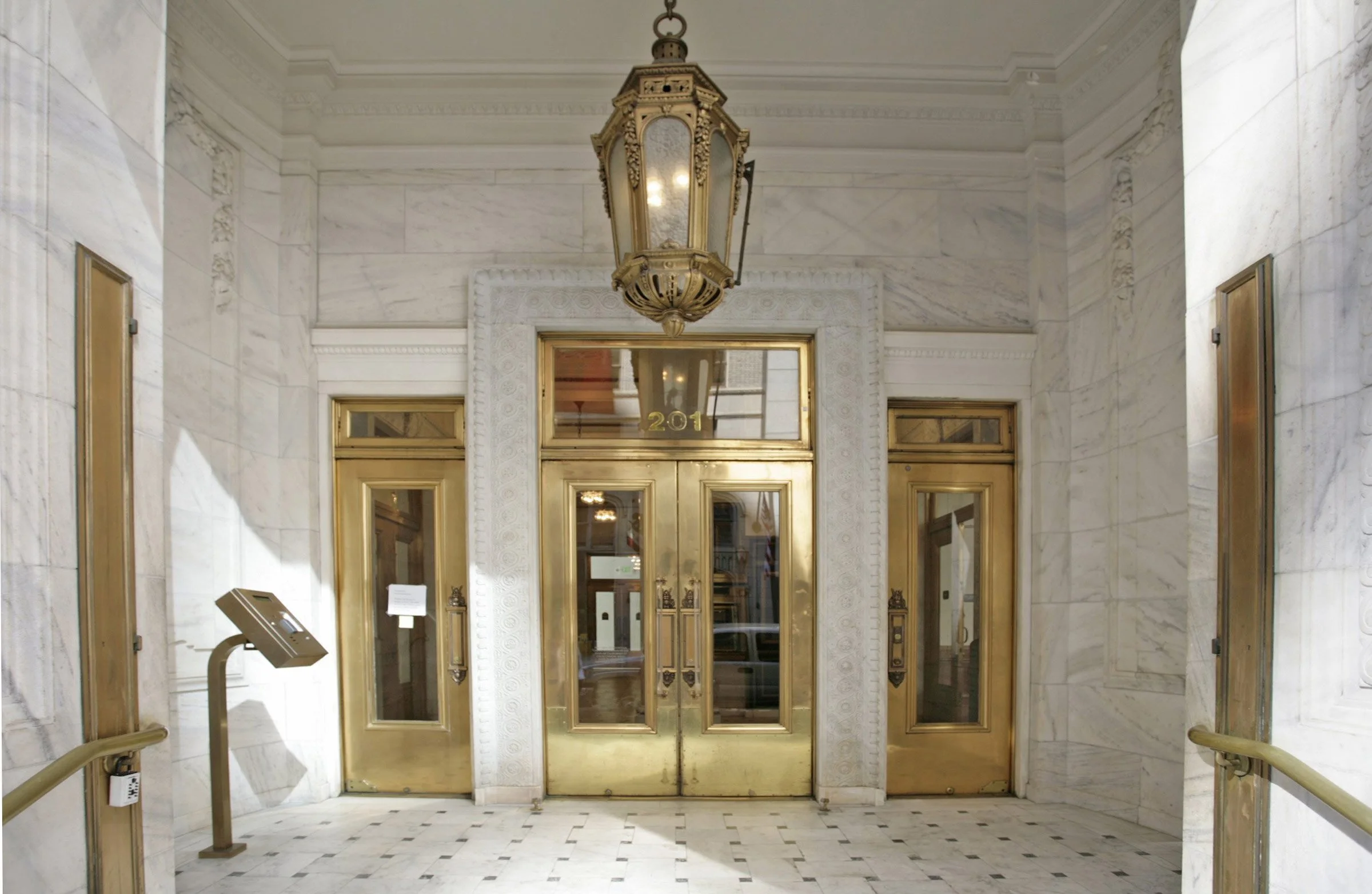 Entrance with gold doors, ornate white marble framing, and a large hanging lantern, labeled with the number 201.