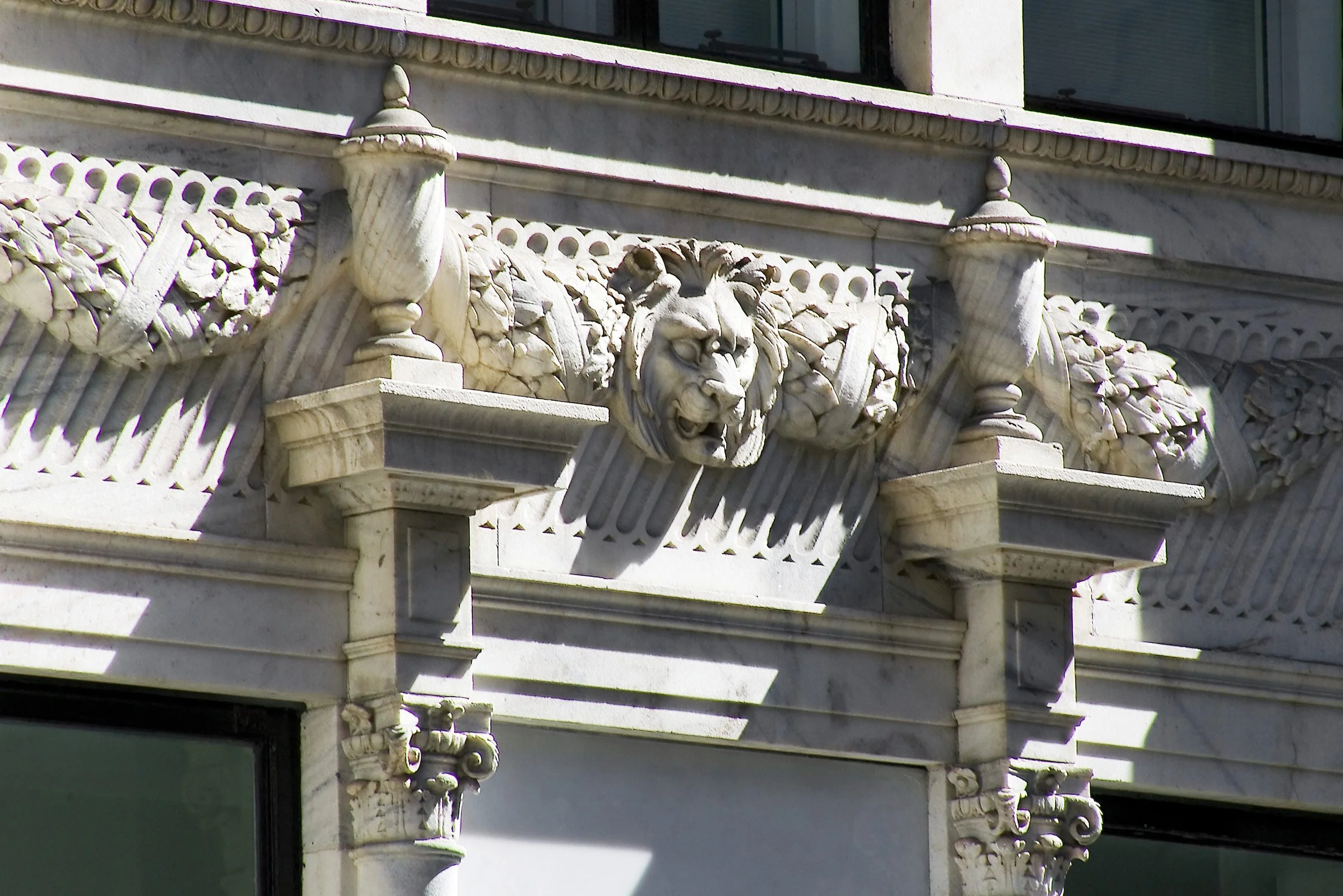 Marble architectural detail featuring a lion's head sculpture on a classical building exterior with ornate carvings and columns.