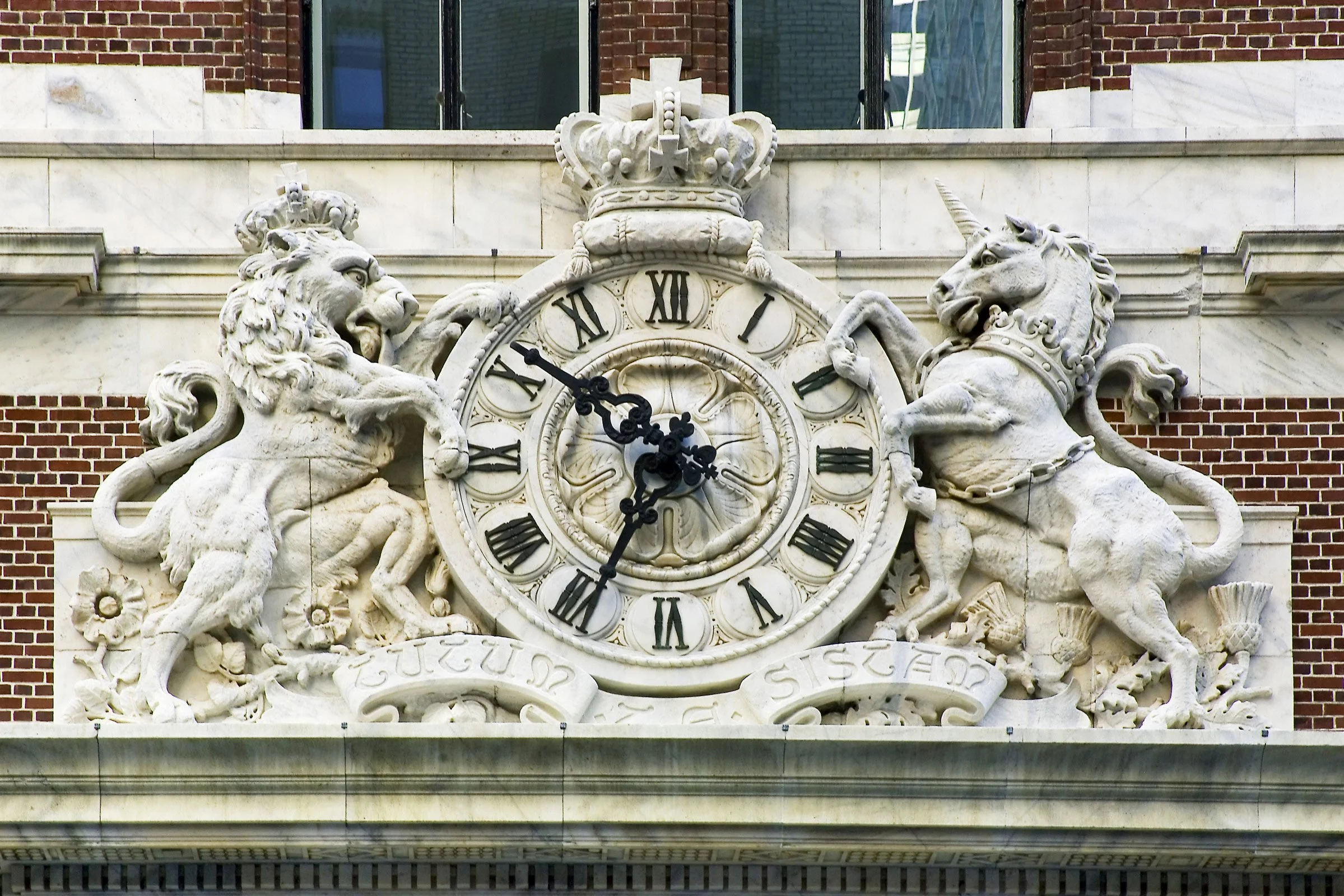 A decorative clock with Roman numerals, flanked by two carved lions and a unicorn, with a crown on top, mounted on an ornate building facade.