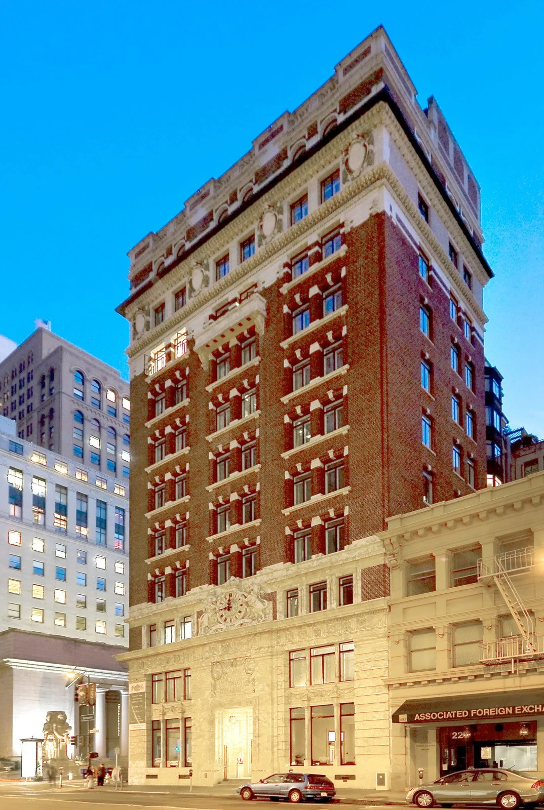 Tall historic brick building with ornate architectural details and multiple levels, located on a city street during twilight.
