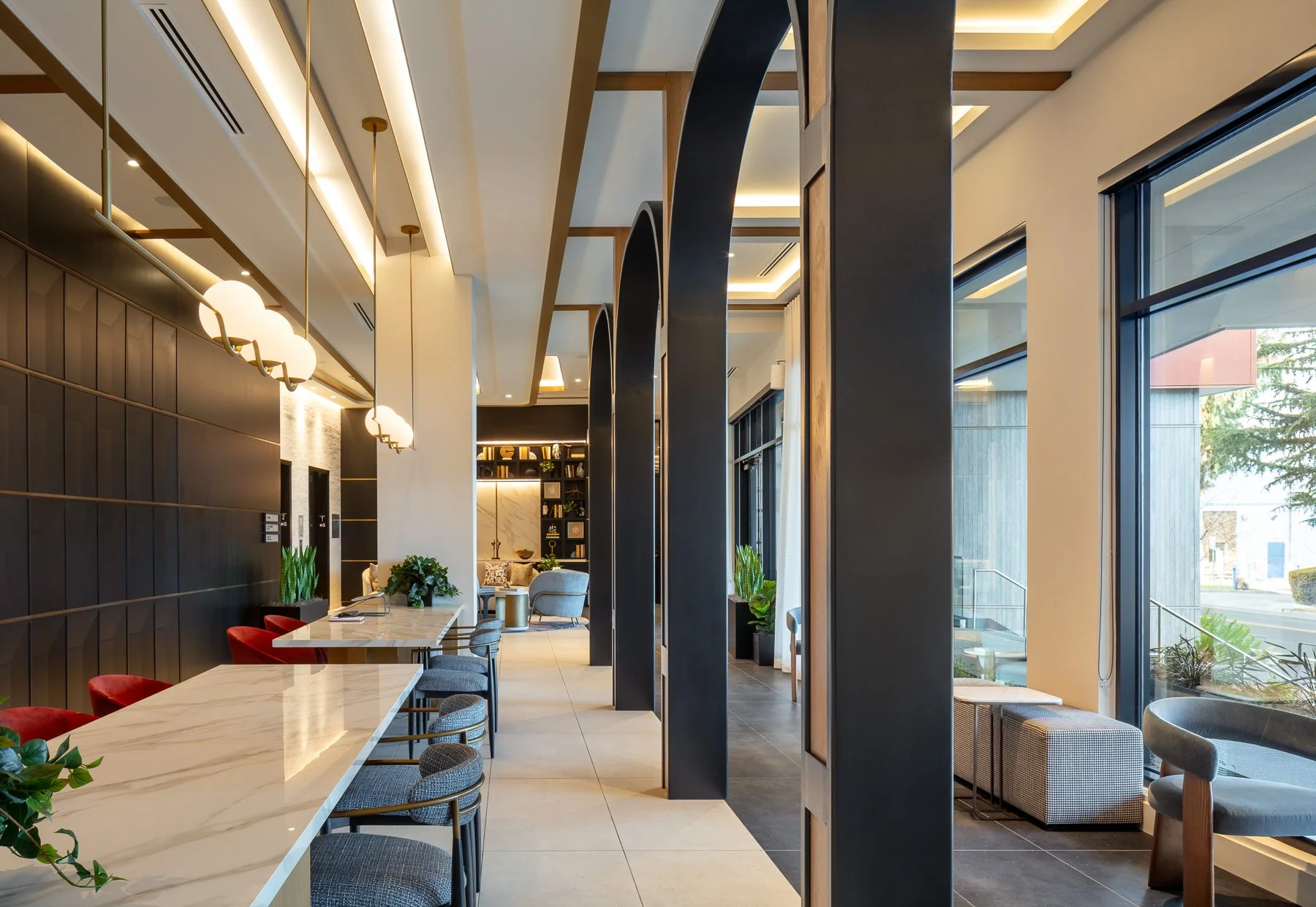 Modern hotel lobby with high ceiling, large windows, and stylish furnishings including chairs, tables, and decorative plants.