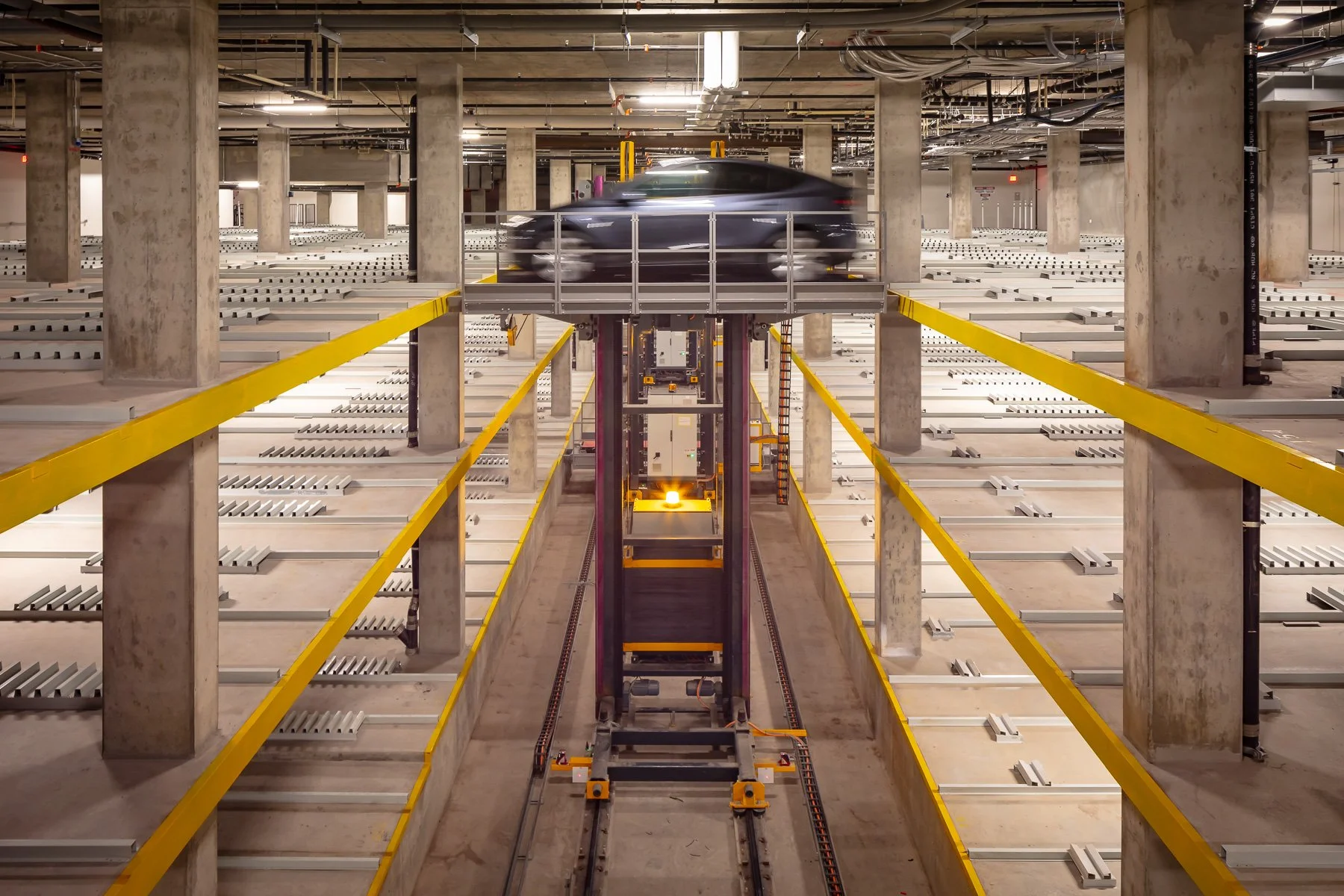 Inside a multi-level parking garage with an autonomous car lift system transporting a black car.