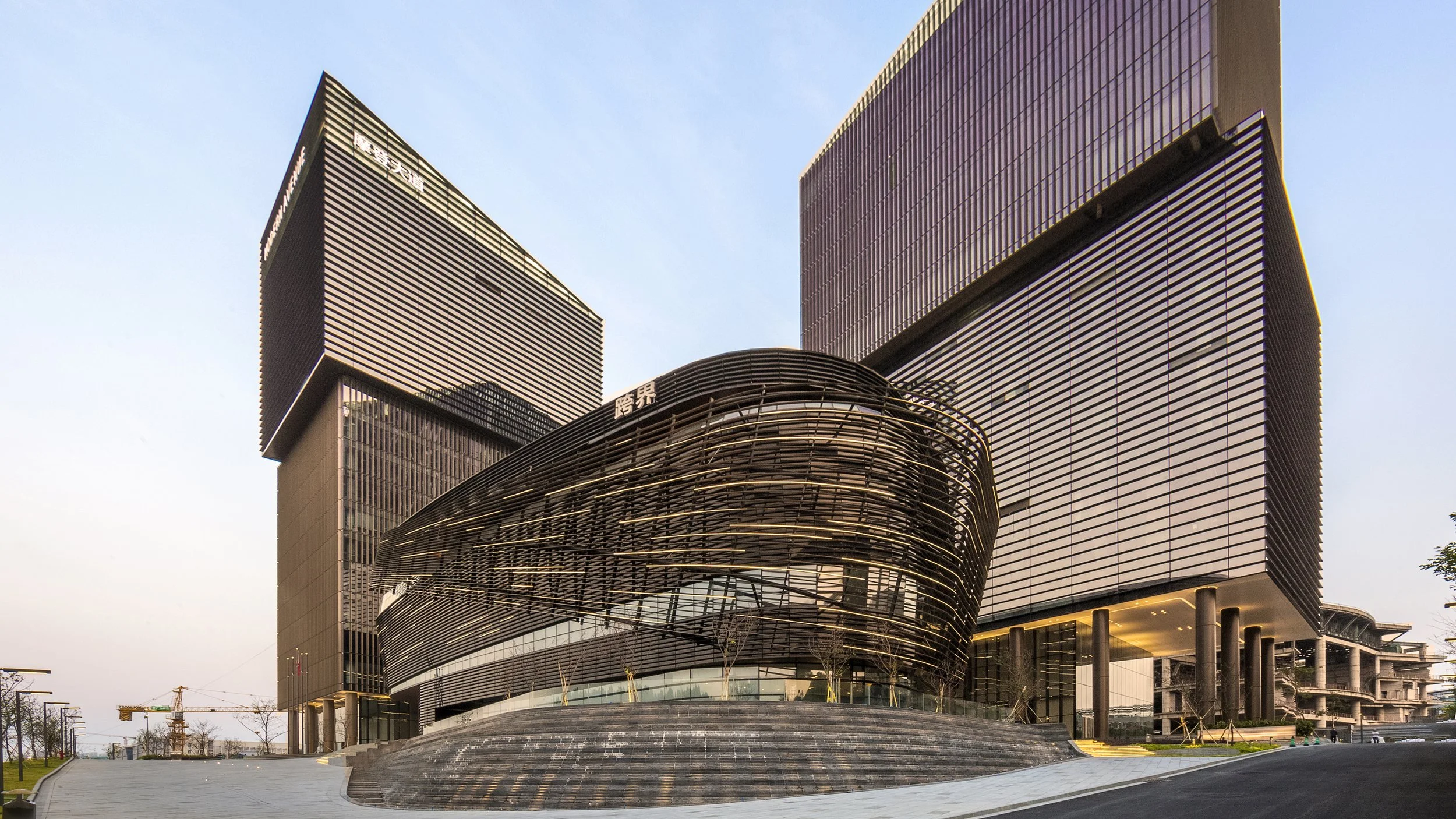 Modern multi-story buildings with sleek glass and dark-colored exteriors in an urban area, with some construction visible in the background.