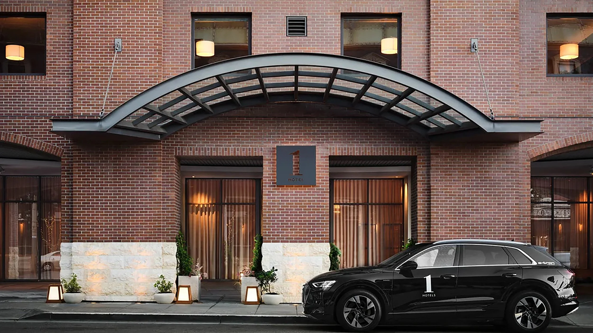 Exterior of a hotel with a brick facade, large windows, and a black luxury vehicle parked in front, adorned with potted plants and outdoor lanterns.