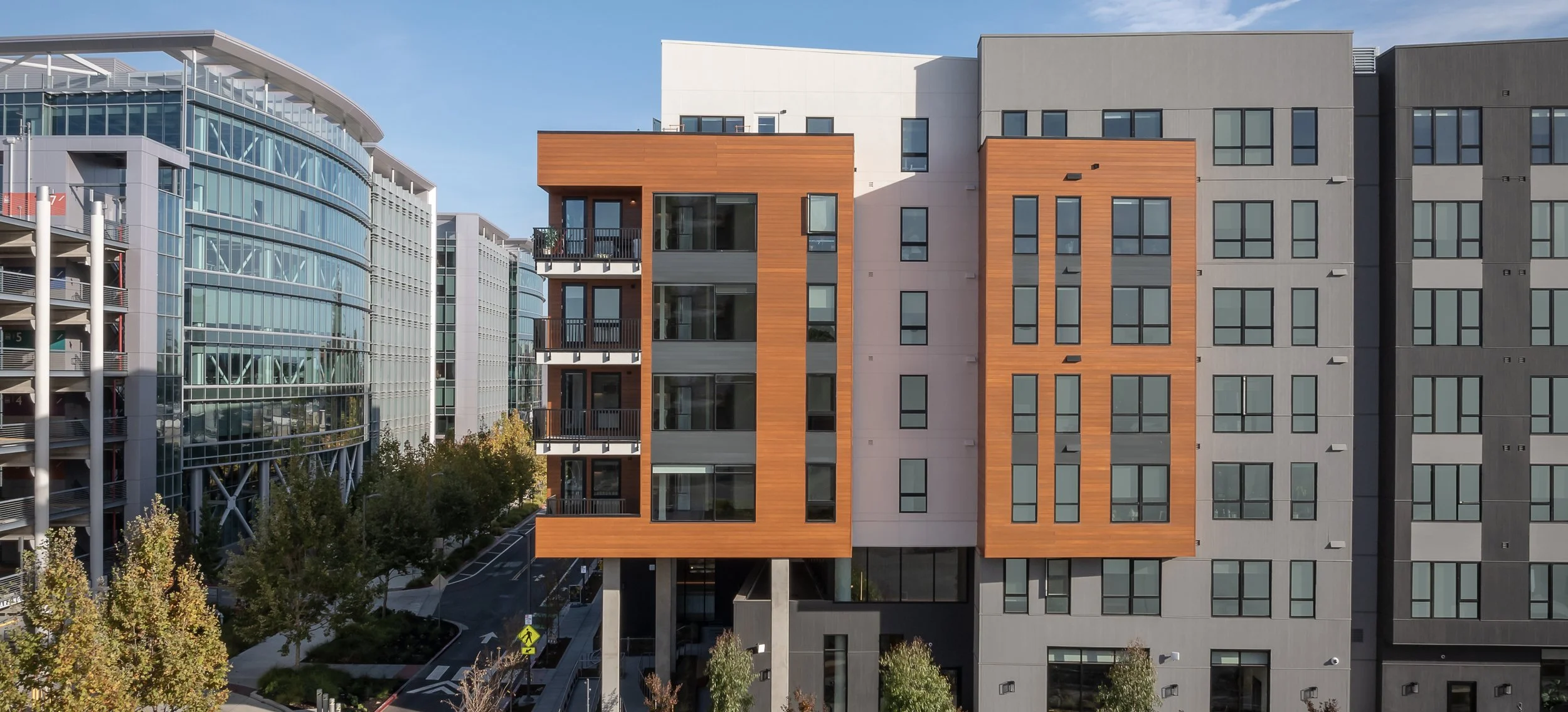 Modern multi-story apartment buildings with glass and wood exteriors and surrounding trees.