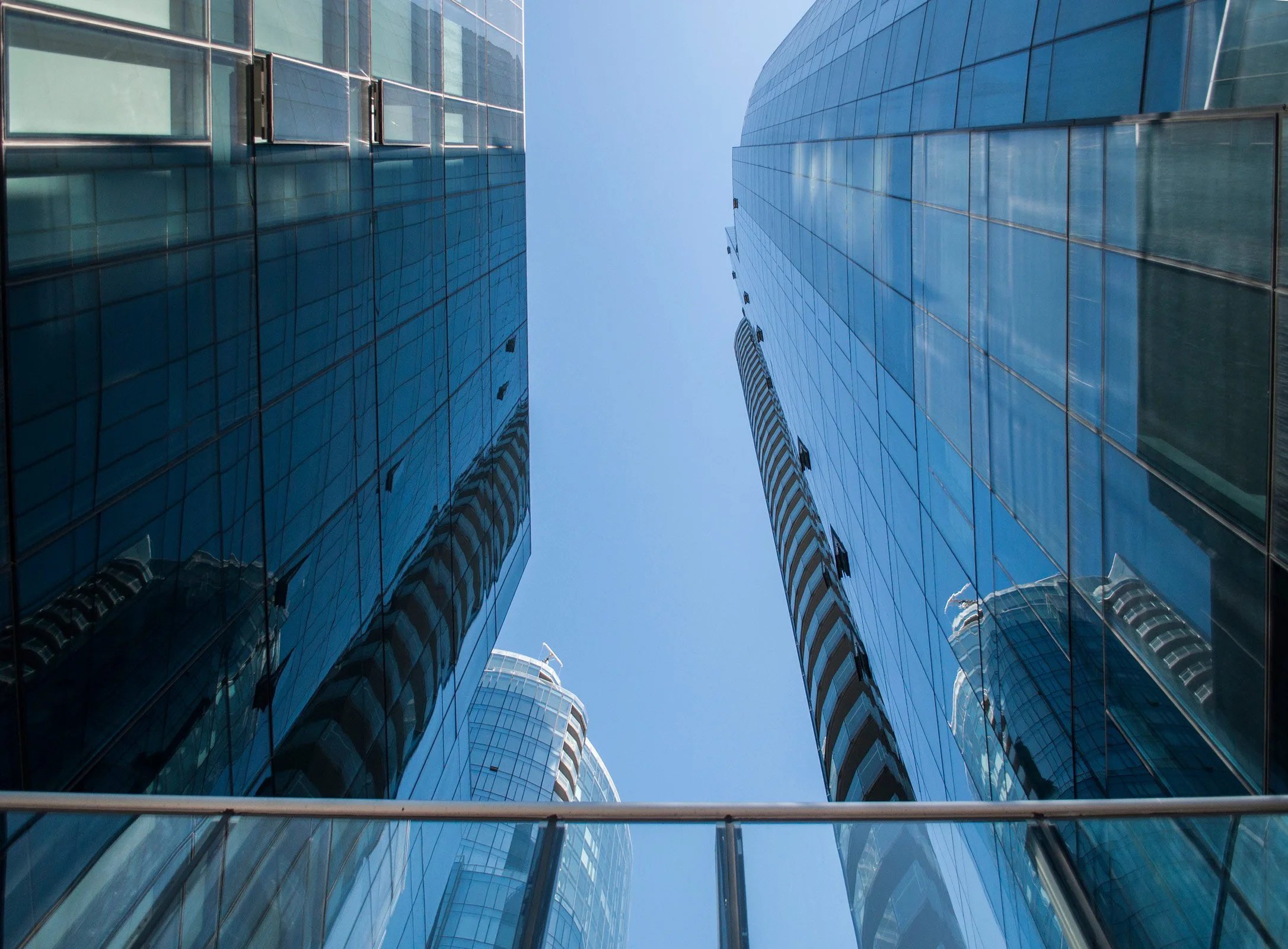 Looking up between two tall glass skyscrapers against a clear blue sky.