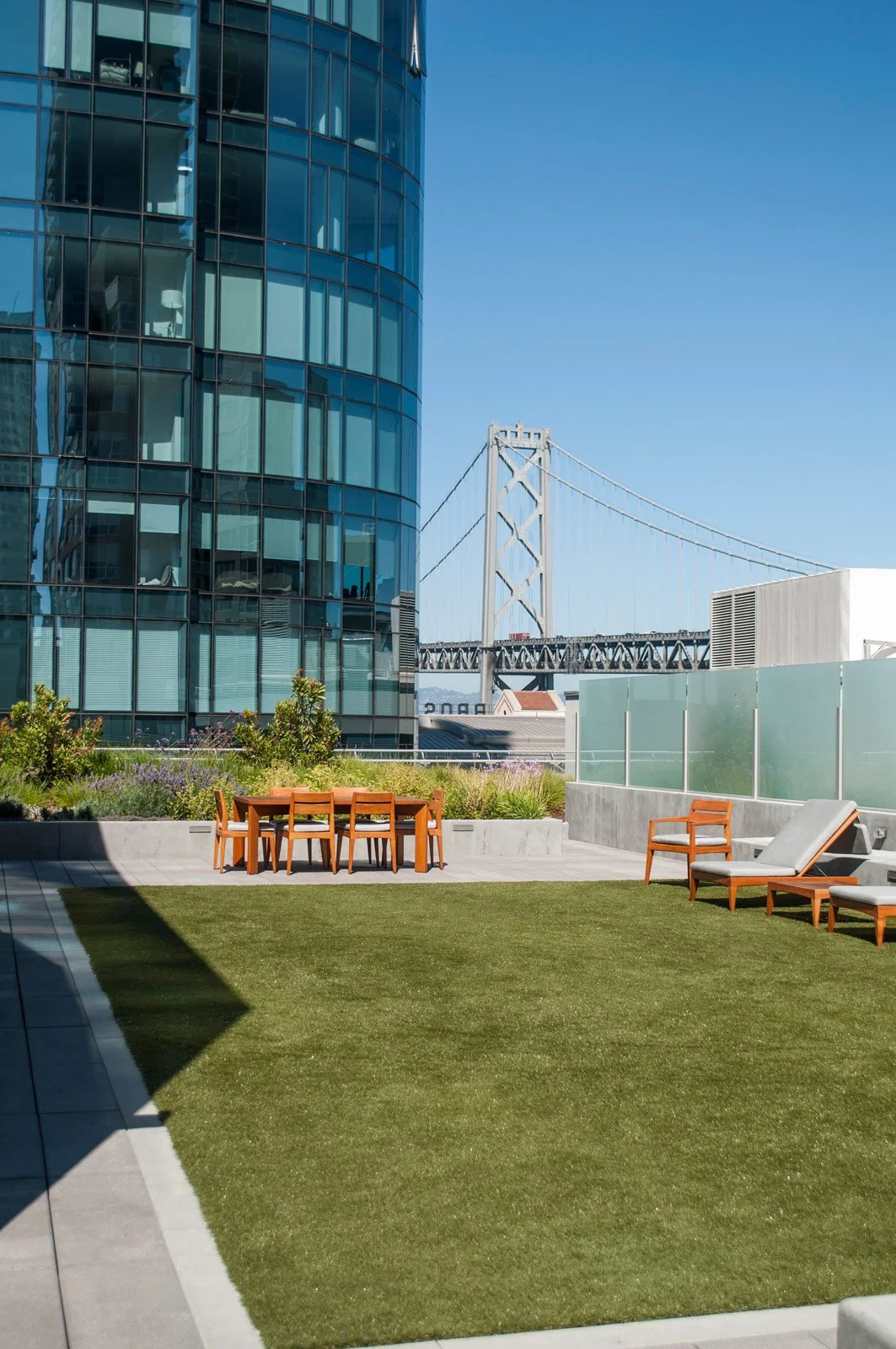 Modern rooftop patio with outdoor furniture and view of a large glass building and bridge.