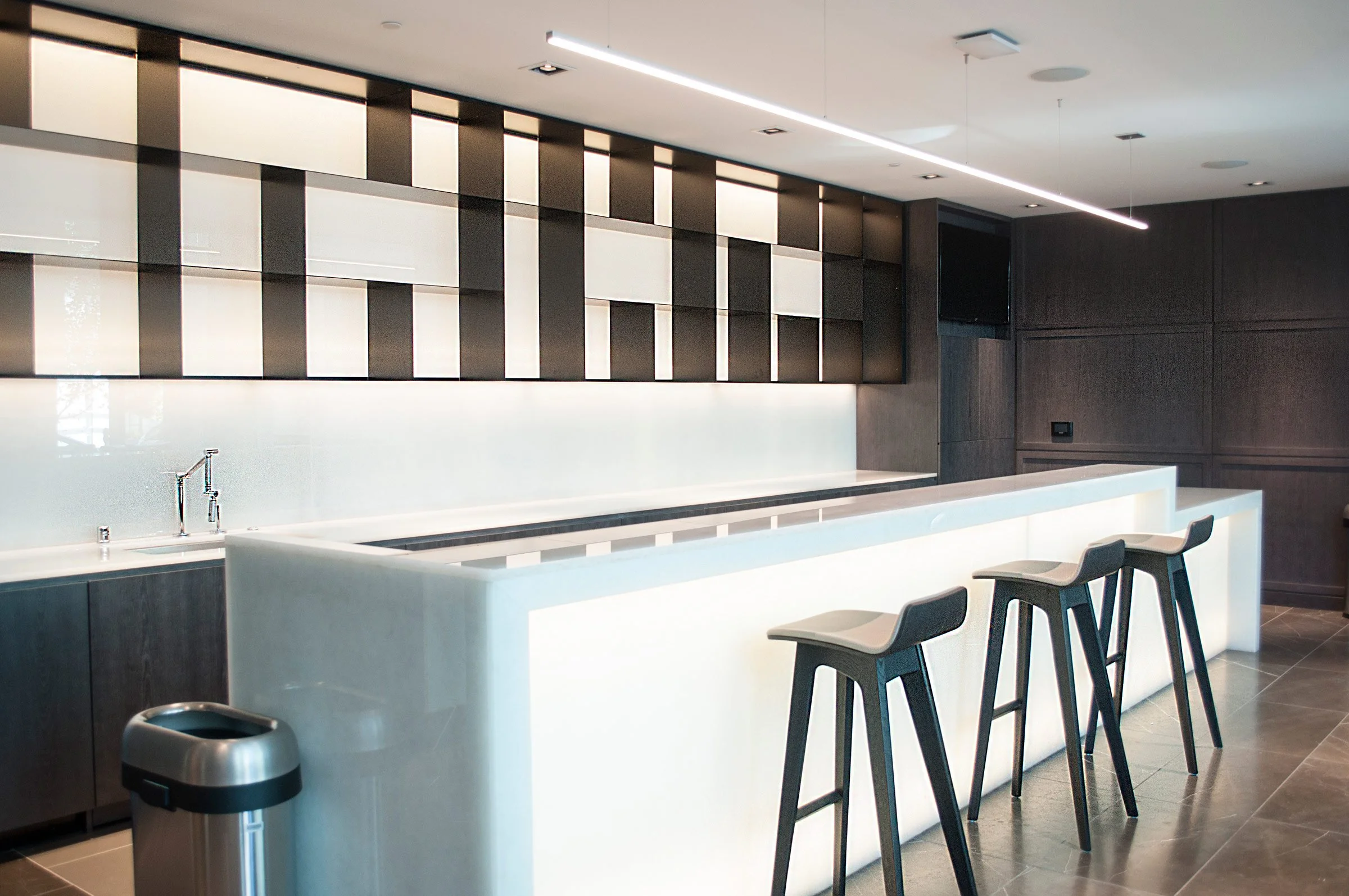 Modern kitchen or bar with a white countertop, three bar stools, dark wood cabinetry, and a geometric patterned black and white wall