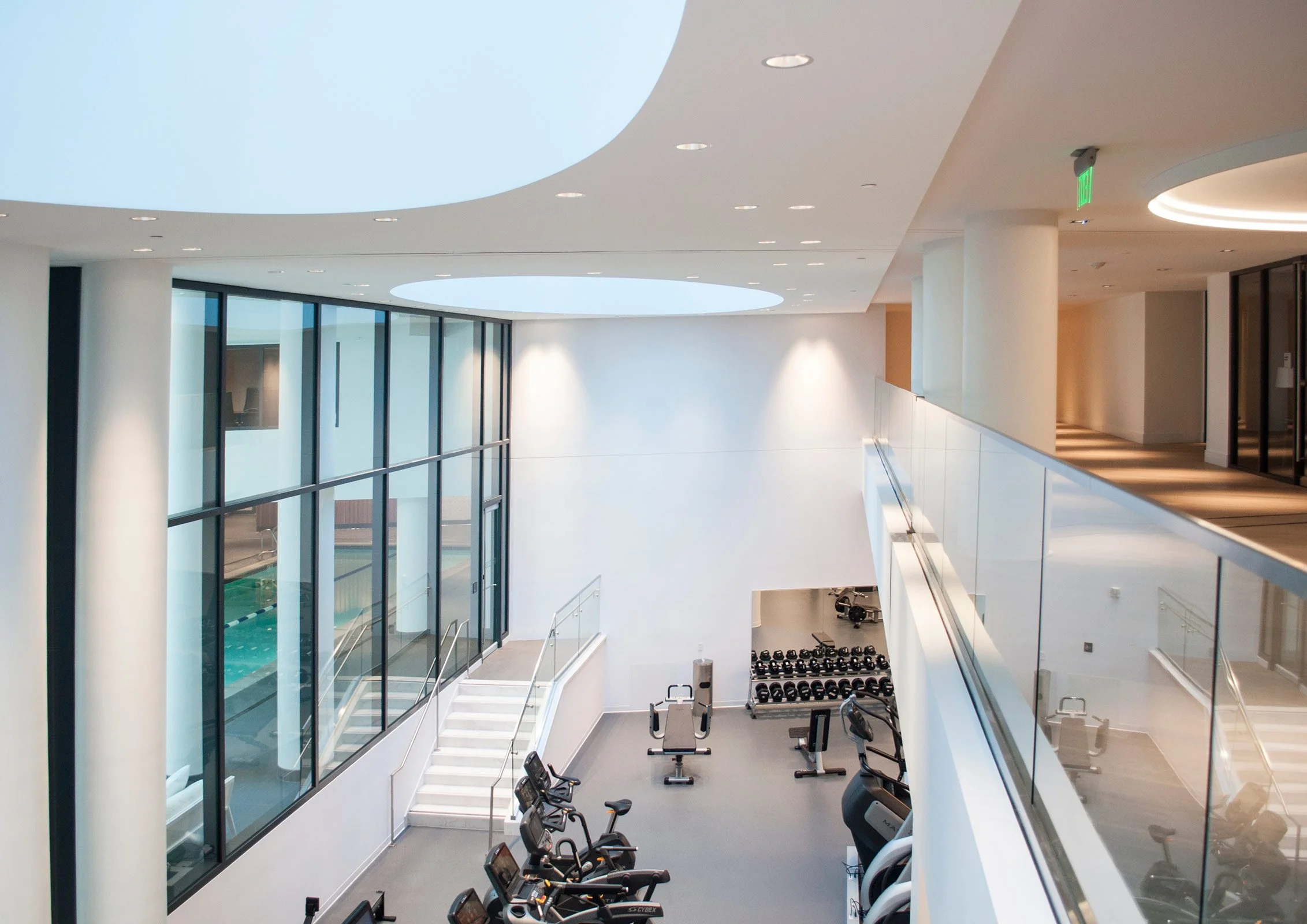 Modern fitness center with gym equipment, exercise bikes, and free weights inside a bright, spacious, and minimalist facility with large windows.