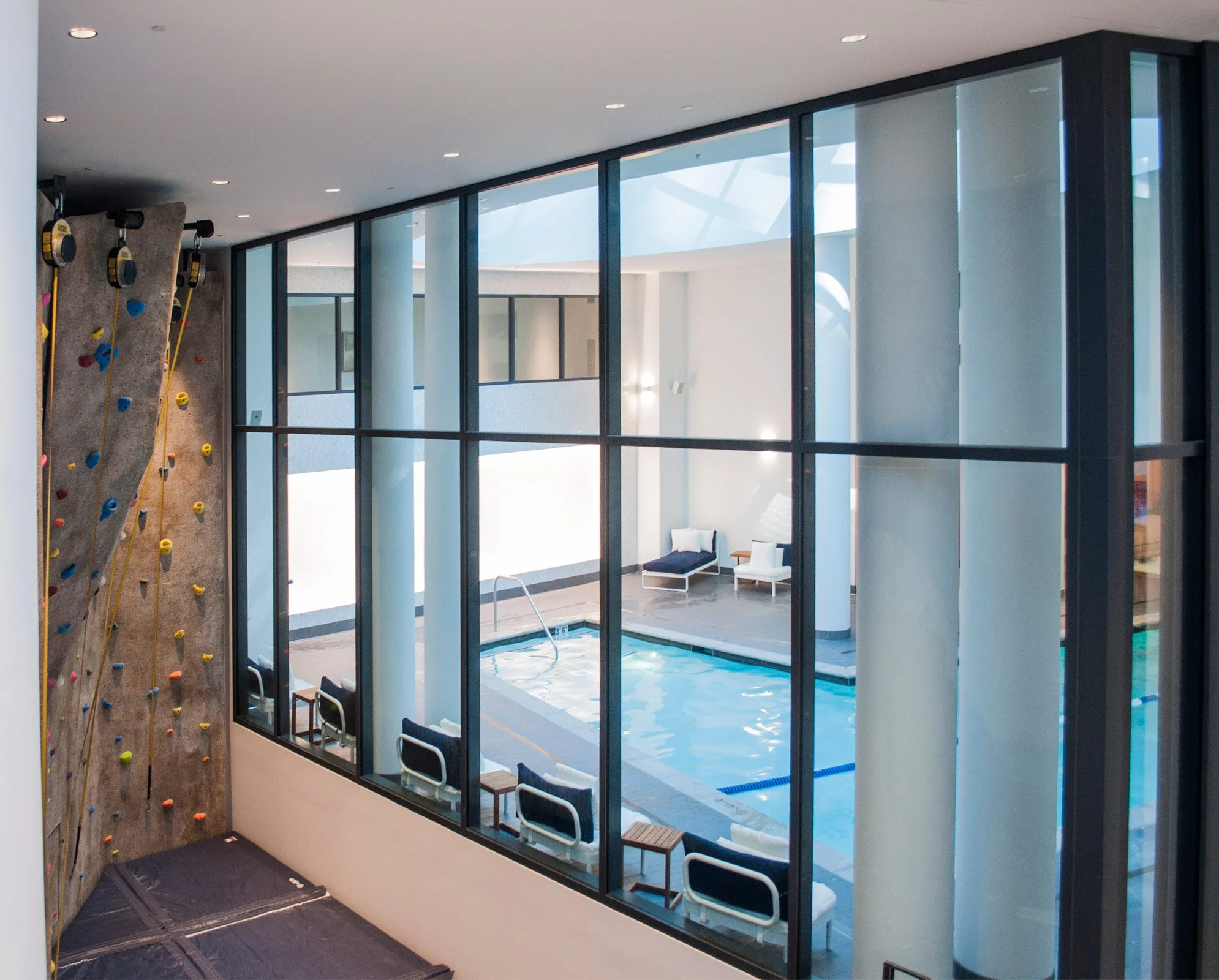 Indoor climbing wall and swimming pool area with lounge chairs visible through large glass windows.