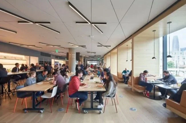 People dining inside a busy modern restaurant or cafe with large windows and wooden interior design.