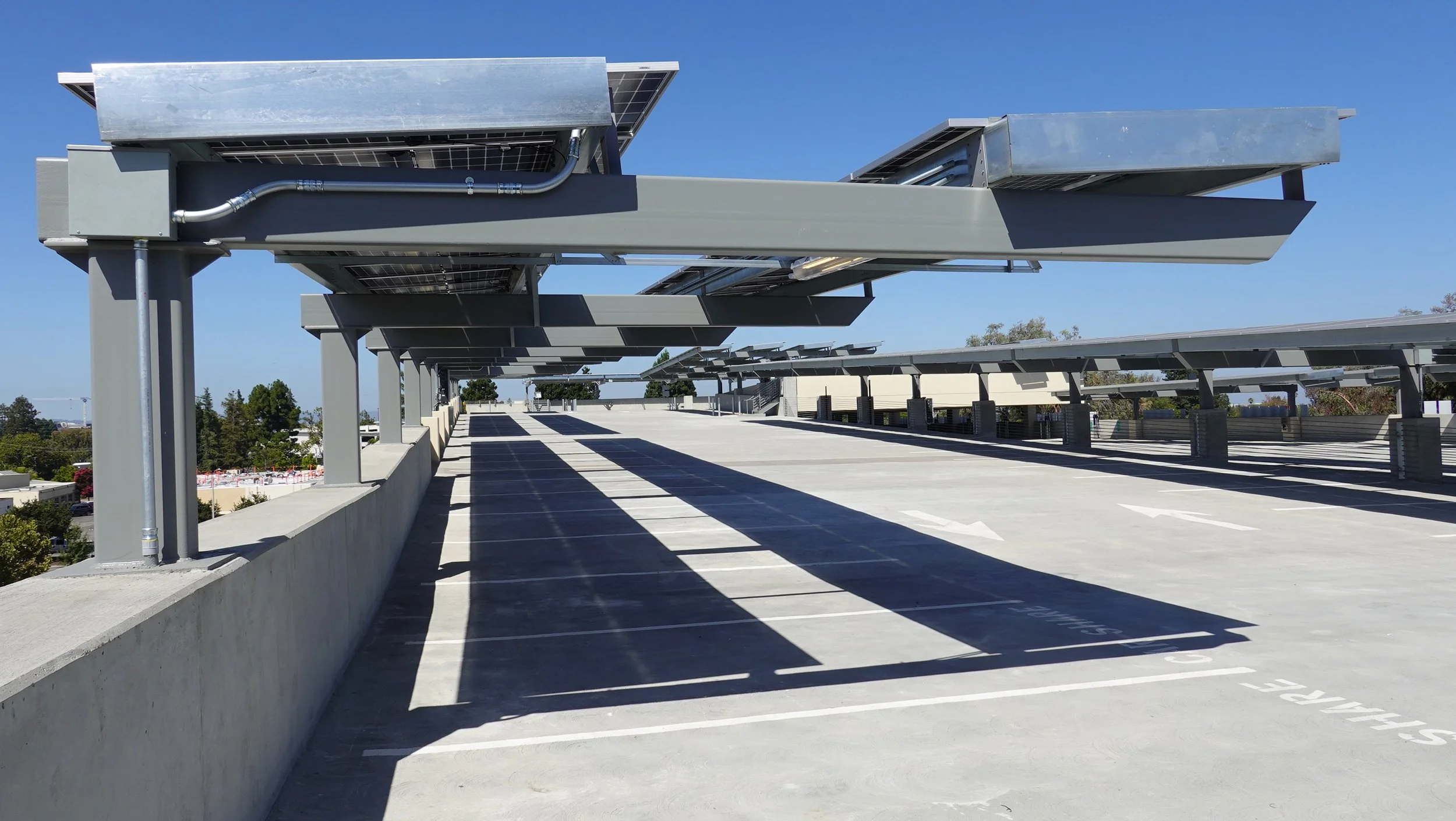Empty parking garage rooftop with solar panel shading structures and outdoor parking spots under clear blue sky.