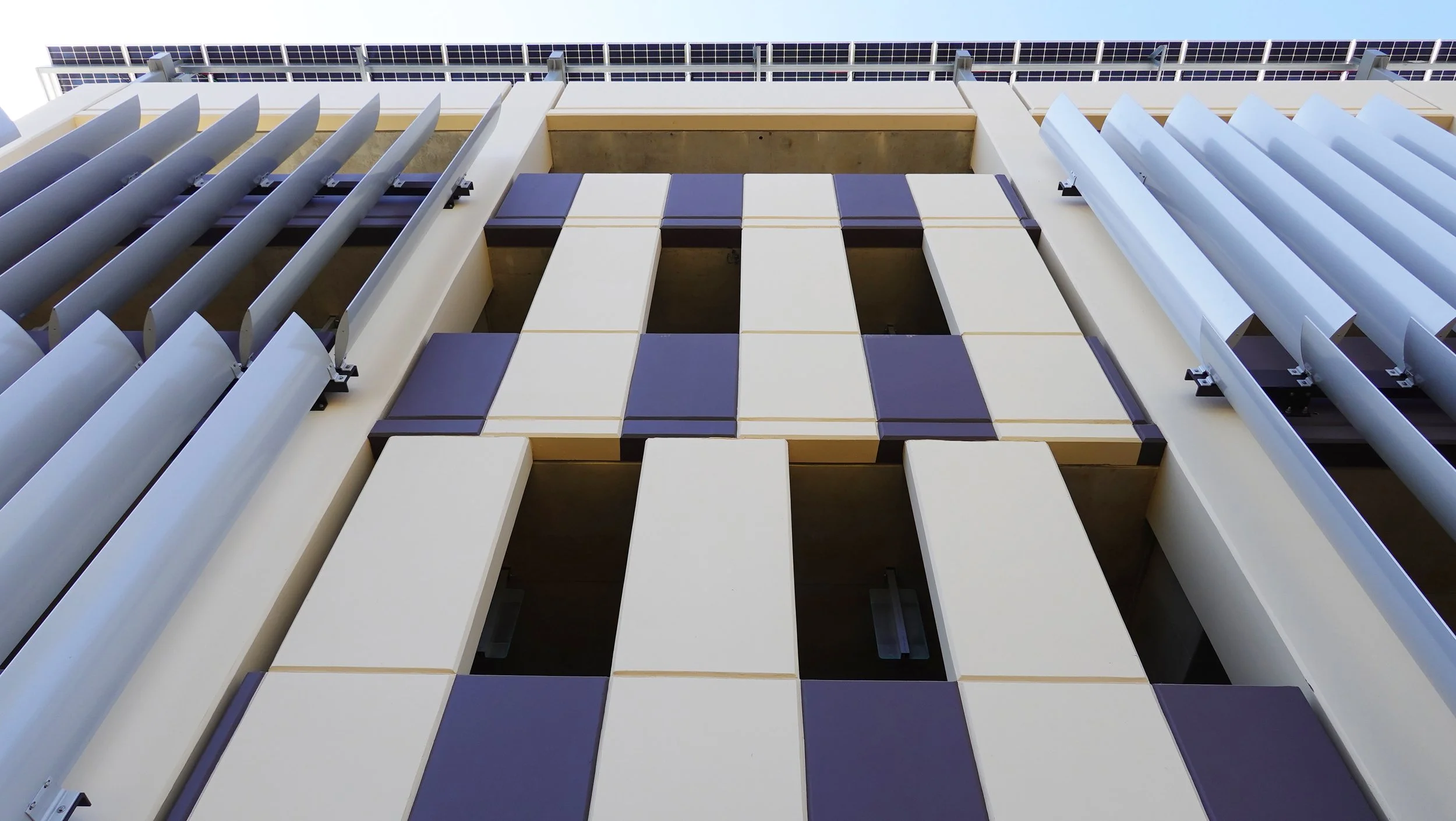 Close-up view of a modern building facade with decorative panels, some of which are shaped like chess pieces, with solar panels at the top.