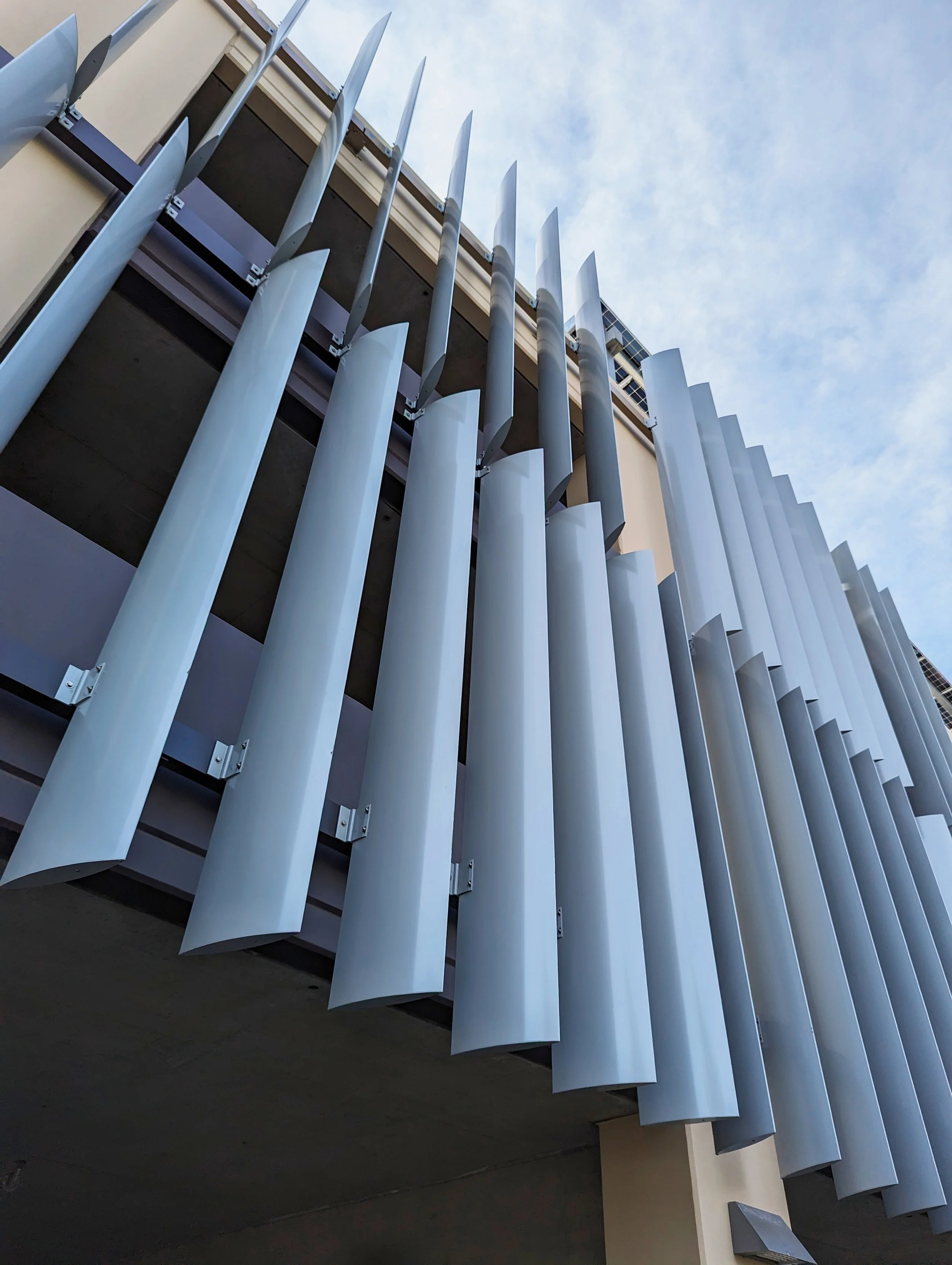 Close-up of modern building façade with vertical metallic louvers against a partly cloudy sky.