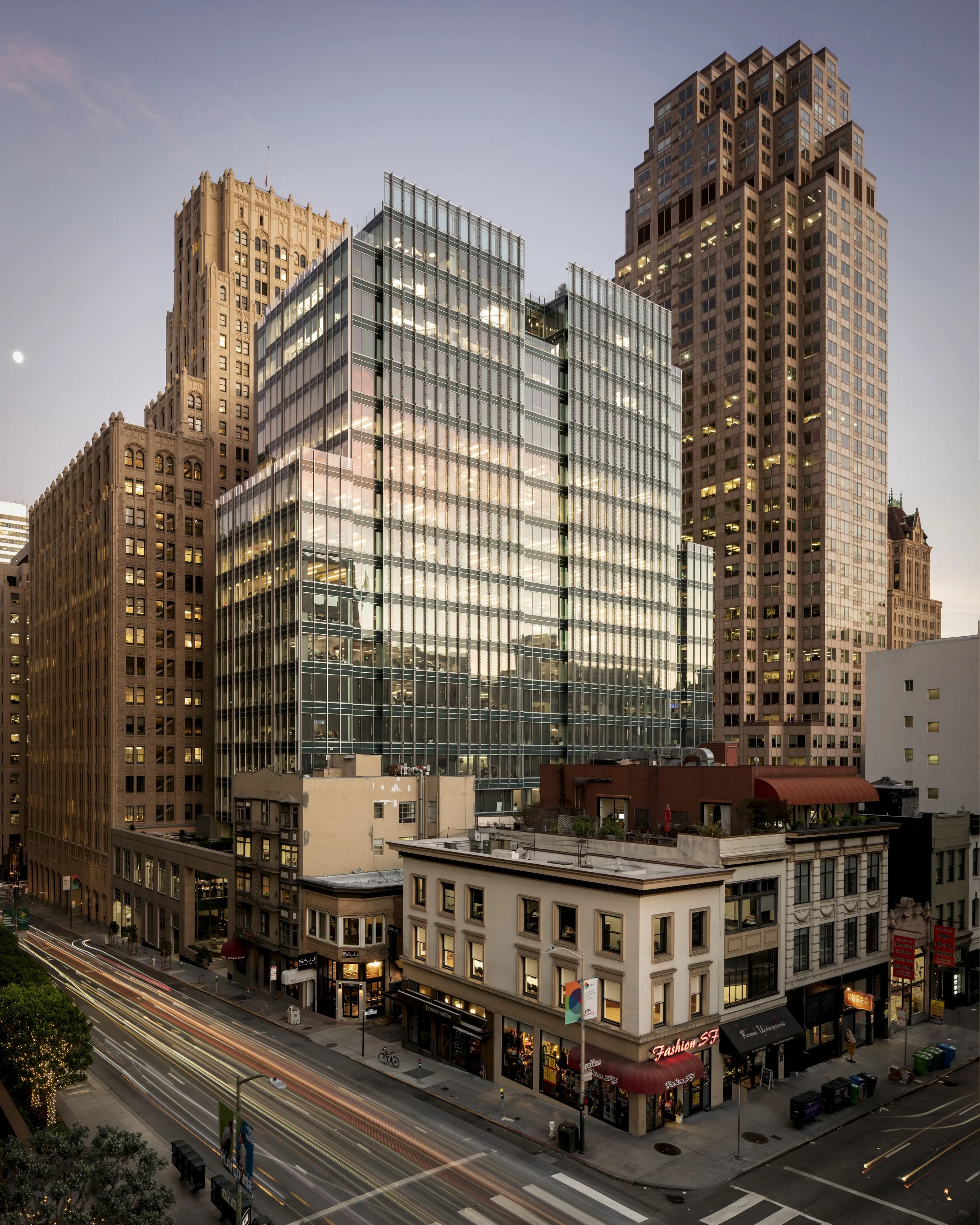 Cityscape of downtown buildings at sunset with light trails from moving vehicles.