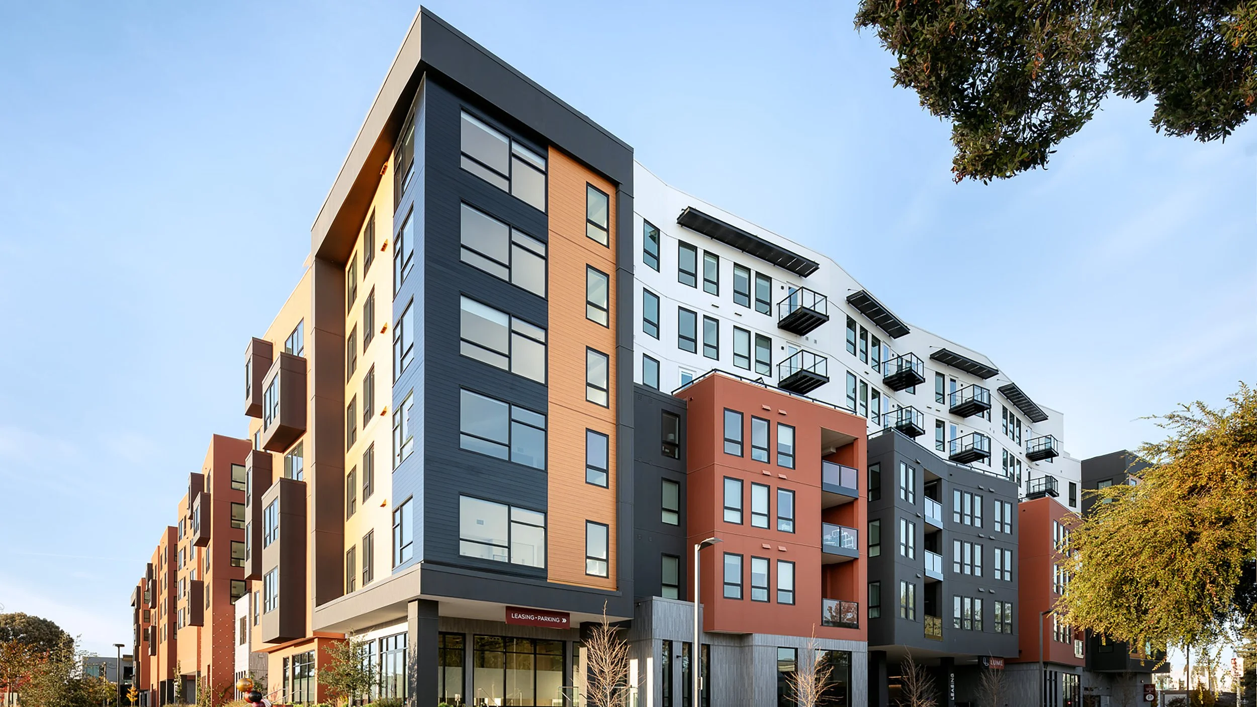 Modern multi-story apartment building with colorful exterior panels, large windows, and balconies against a clear blue sky.