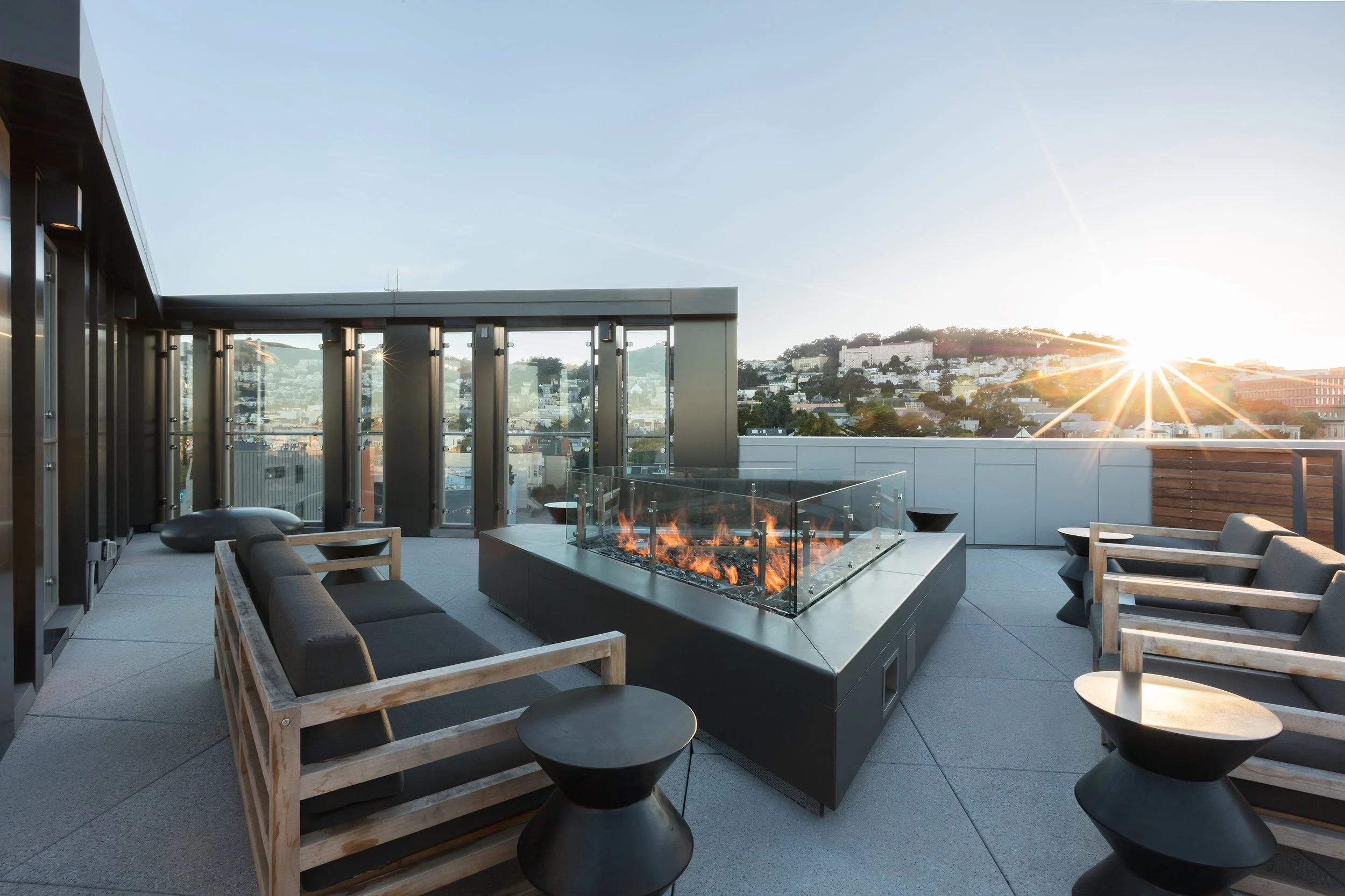 Rooftop terrace with modern outdoor furniture, a fire feature, and a city view at sunset