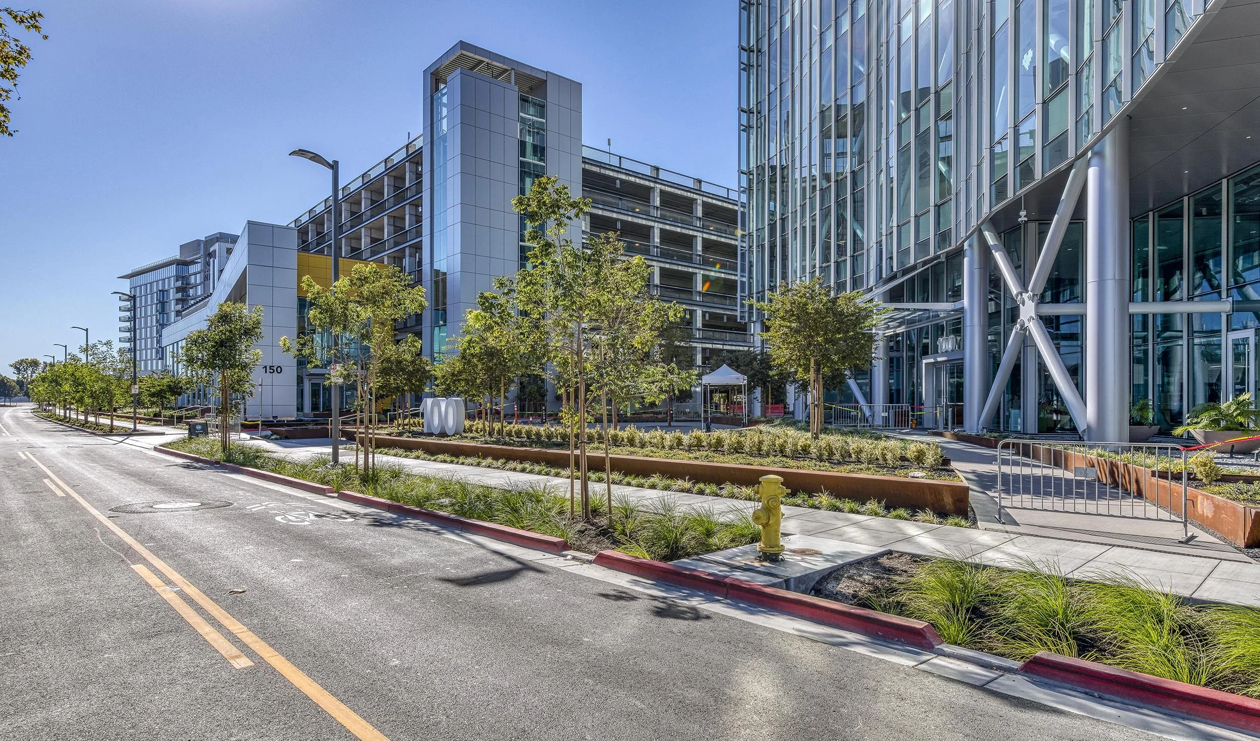 Modern office building with glass exterior, landscaped sidewalk, and street with trees and a fire hydrant.