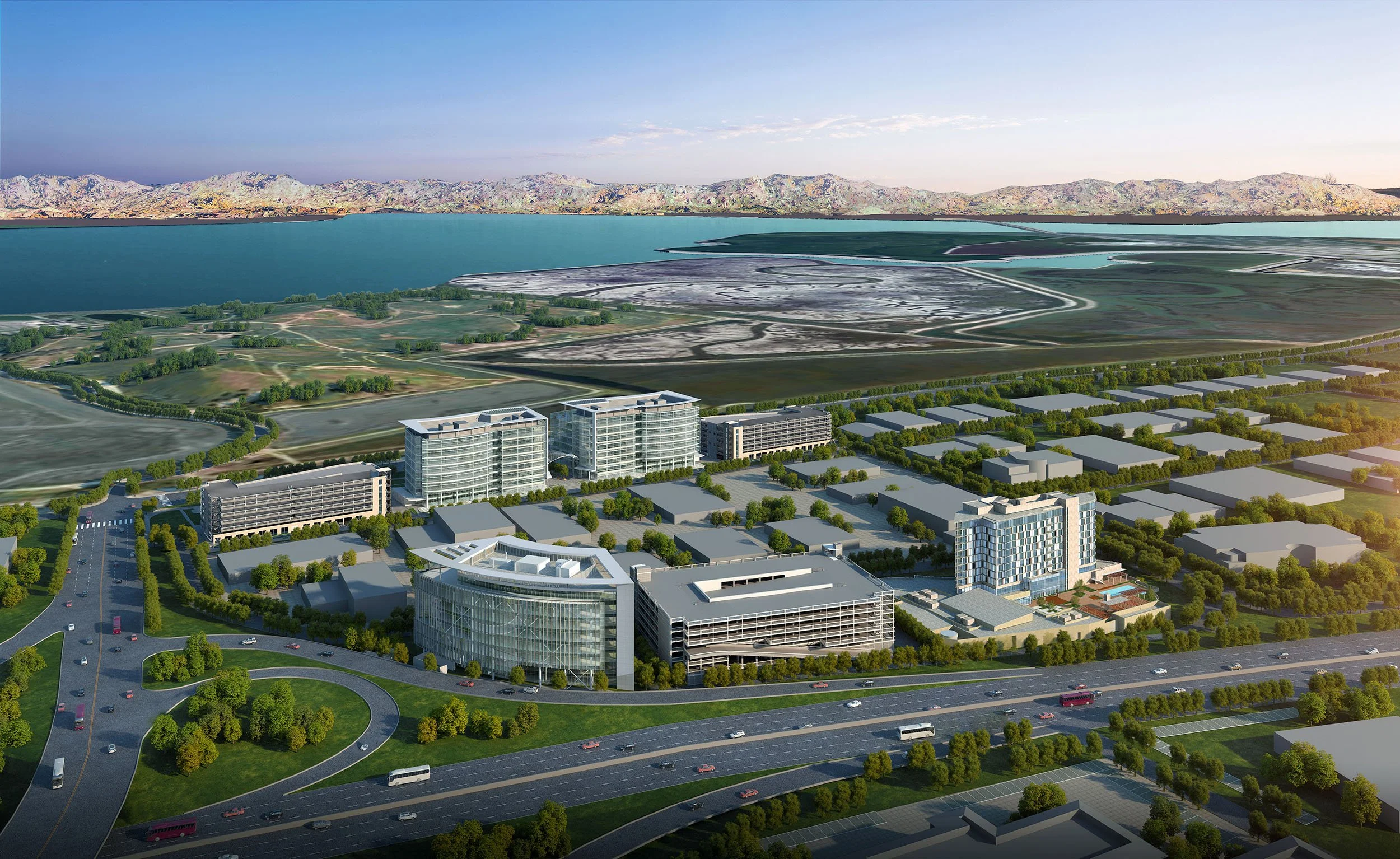 Aerial view of a modern cityscape near a large body of water with mountains in the background, featuring tall glass buildings, roads, and greenery.