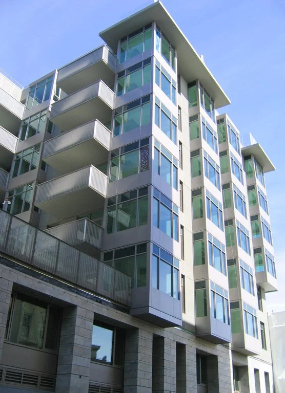 Modern multi-story apartment building with large glass windows and balconies, under a clear blue sky.