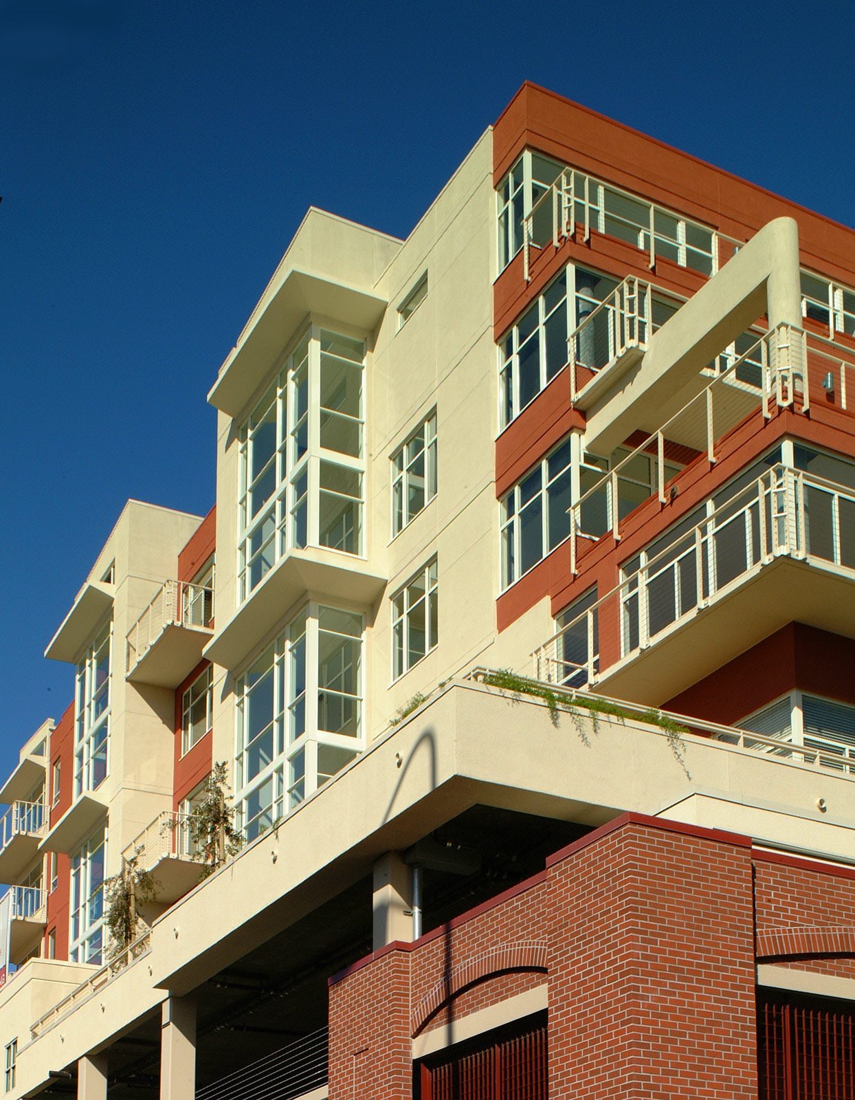 Modern apartment building with large glass windows and balconies, against a clear blue sky.