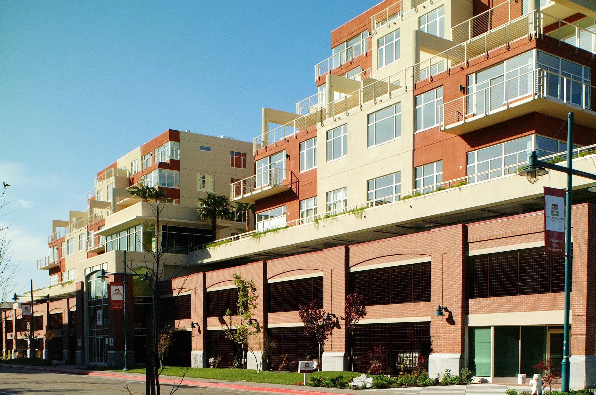 Multi-story modern residential building with balconies, large windows, and brick and beige exterior, under a clear blue sky.