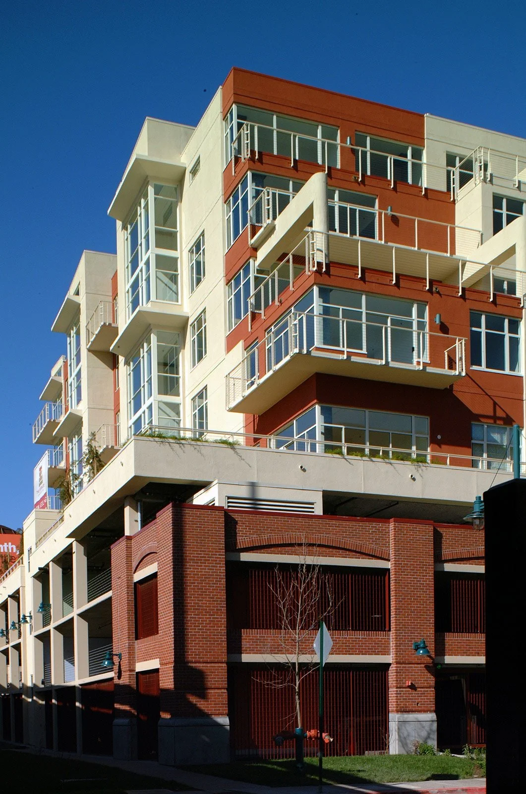 Modern multi-story apartment building with balconies and large windows, featuring a combination of white, red, and brick facade, under a clear blue sky.