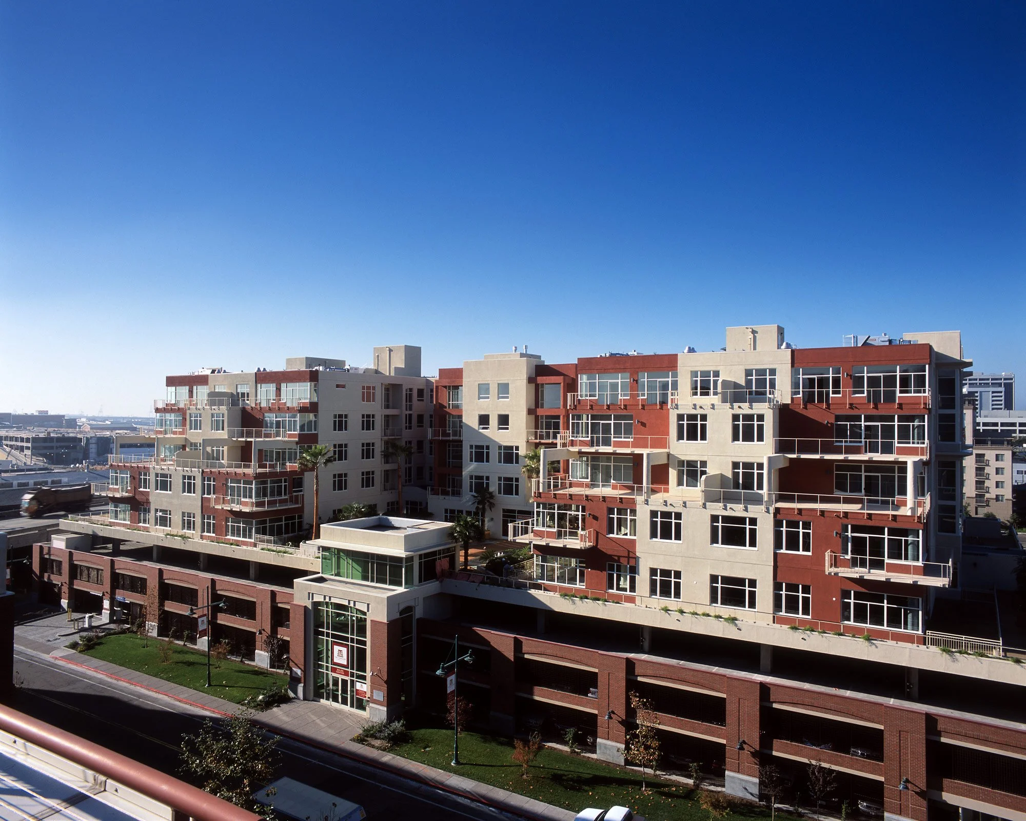 Modern multi-story apartment building with balconies on a city street under a clear blue sky.