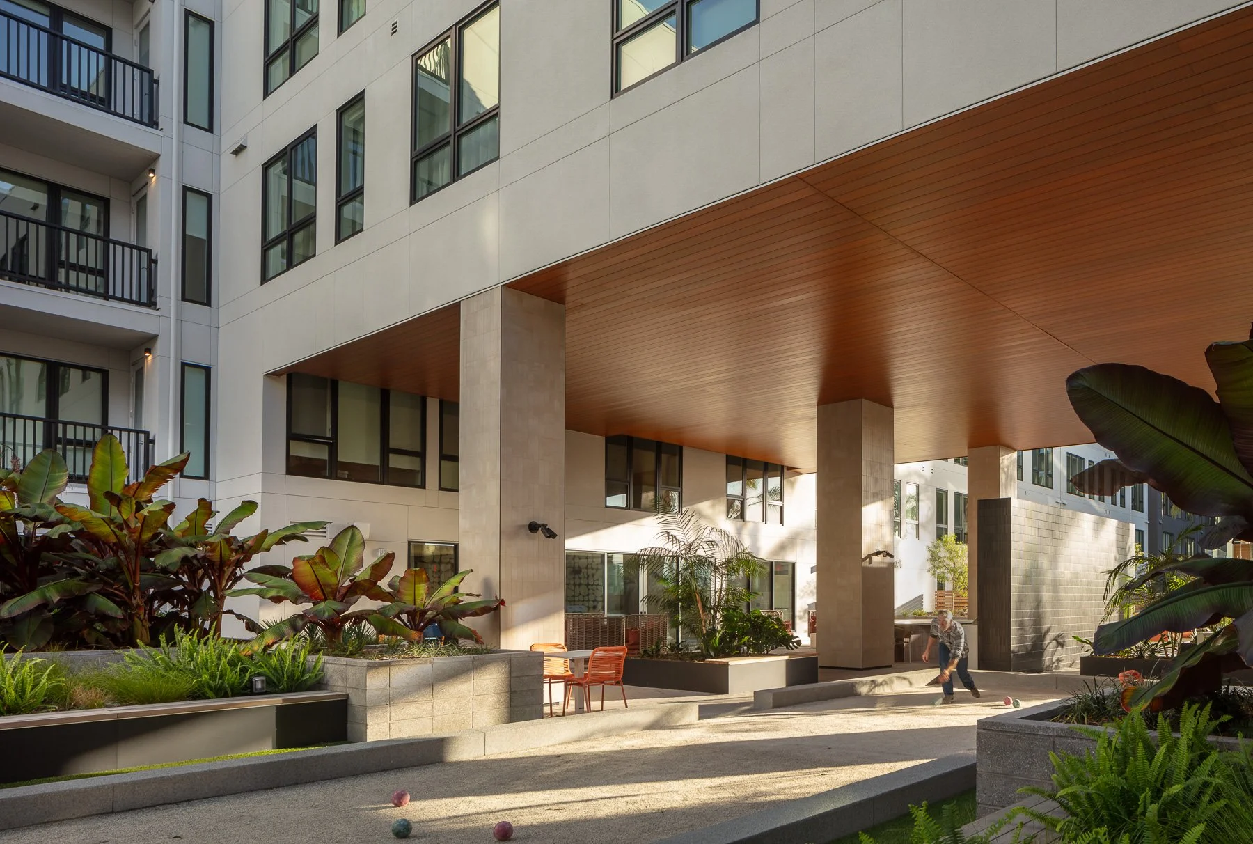Outdoor patio area of a modern apartment complex with seating, plants, and a person playing a game with balls.