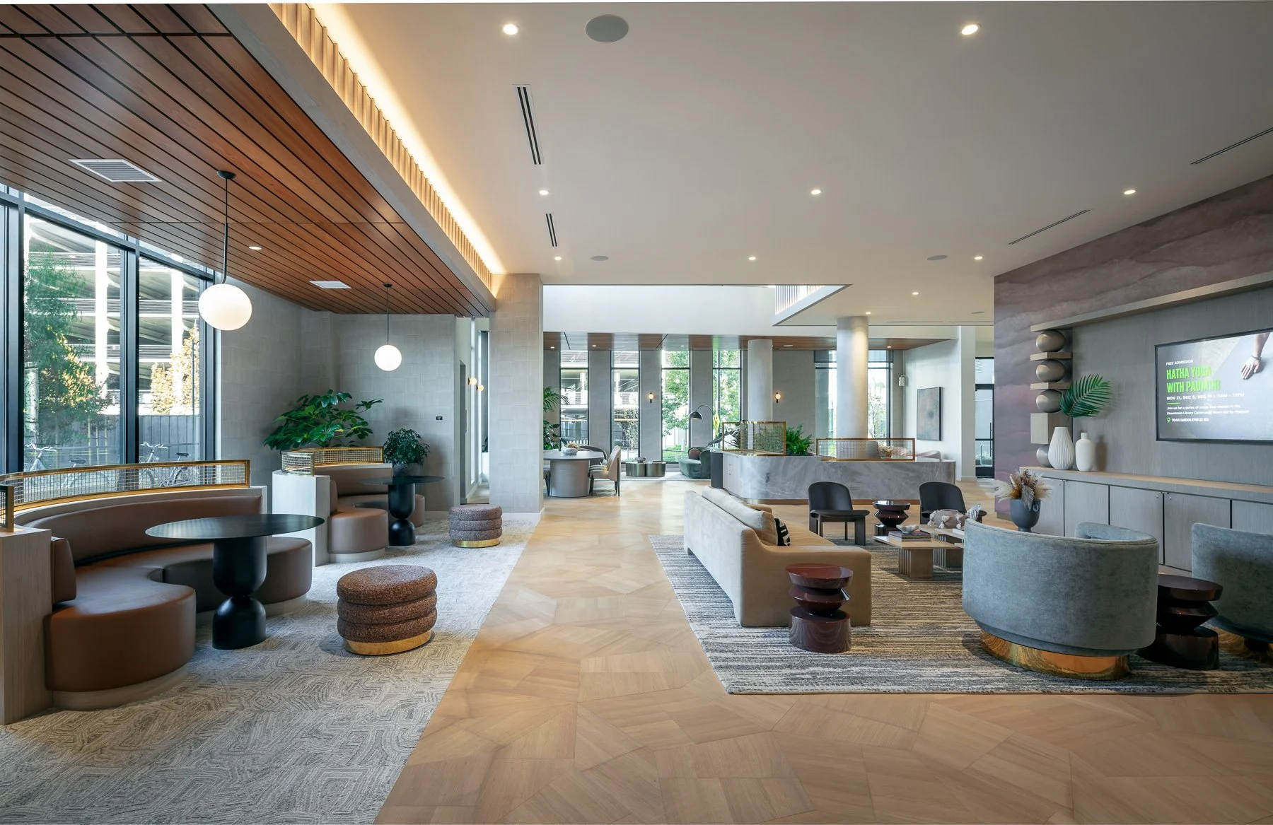Modern hotel lobby with natural light, contemporary furniture including sofas and armchairs, decorative plants, and wall art, creating a welcoming lounge area.
