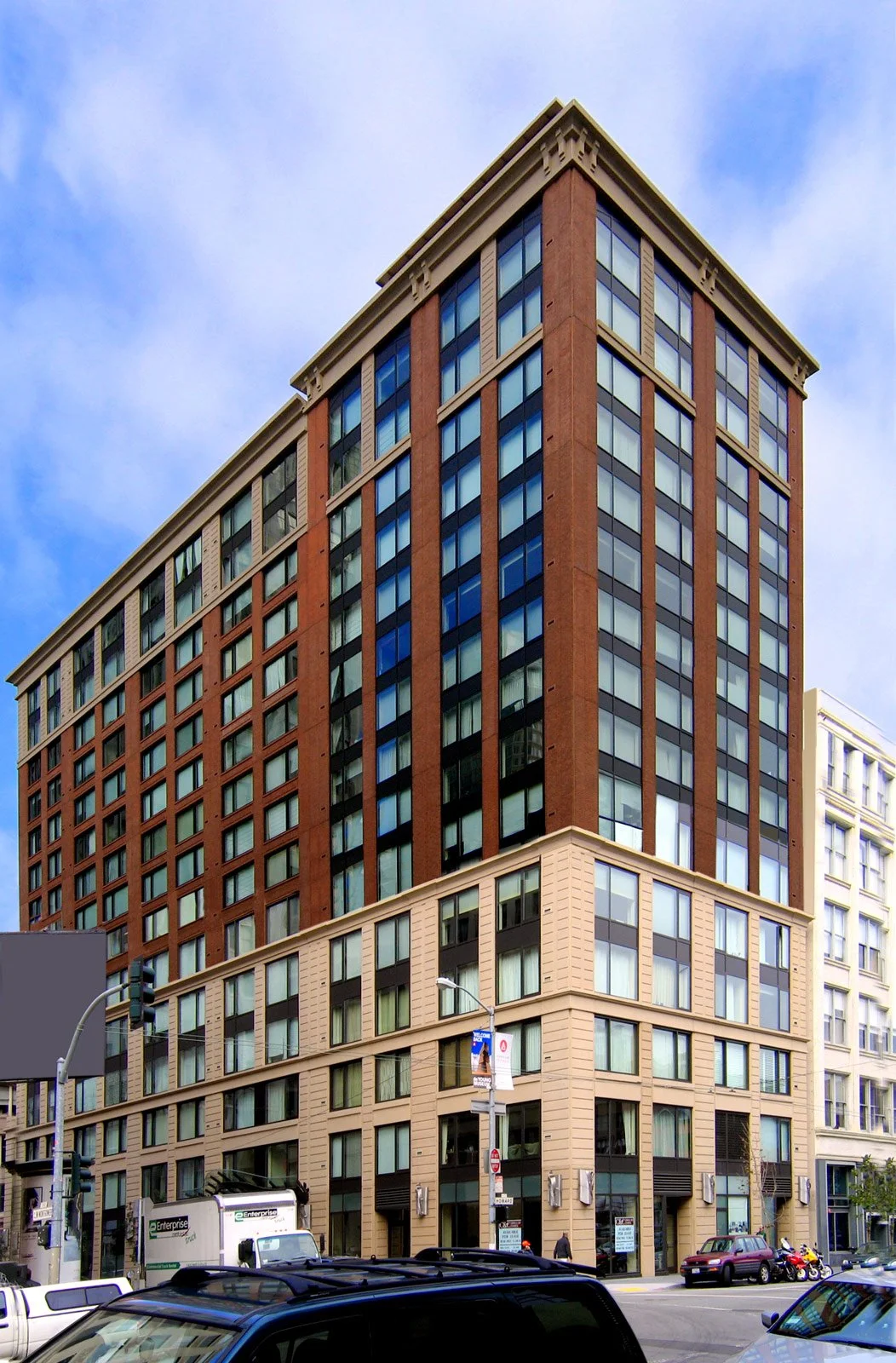 A modern multi-story building with a brick and glass exterior, situated on a busy street corner with cars and pedestrians.