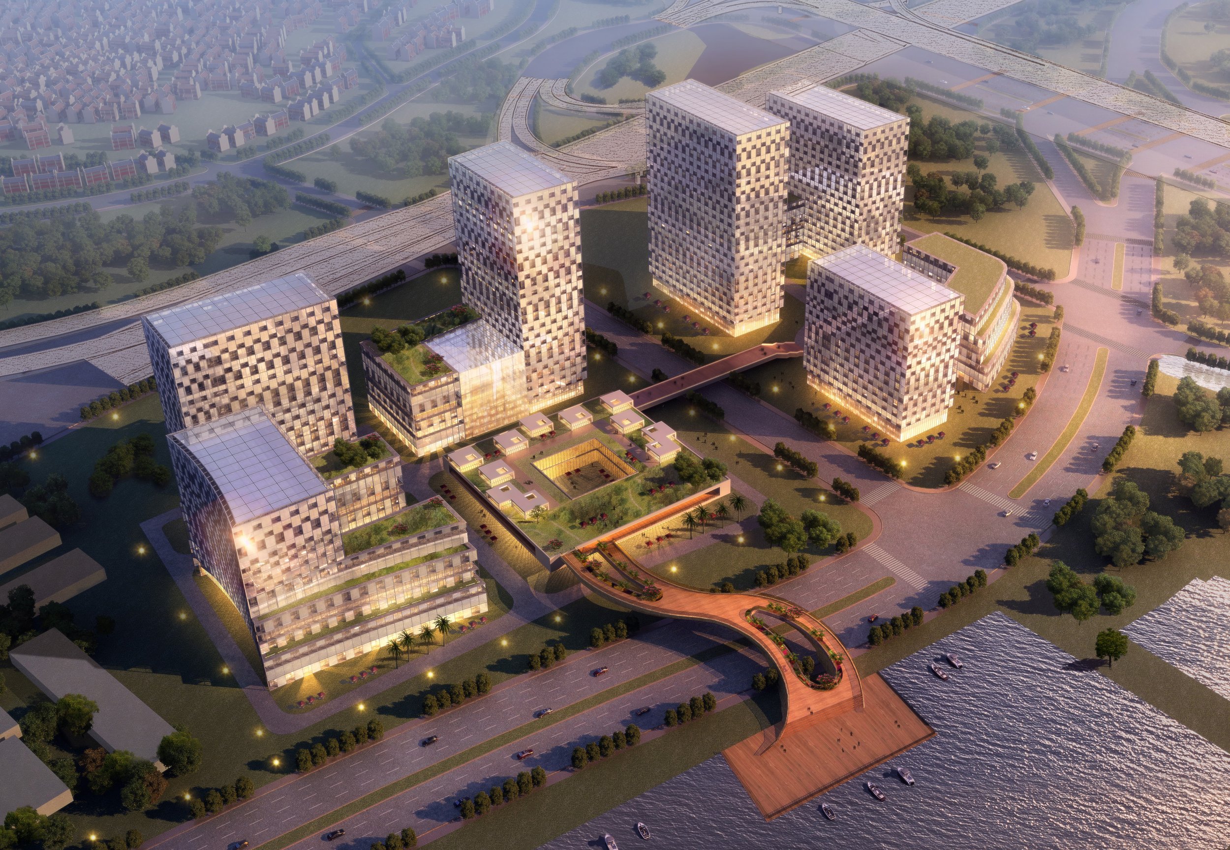 A modern urban development with several multistory buildings, landscaped gardens, a bridge, parking lots, and a waterfront area, depicted in an aerial view during sunset.