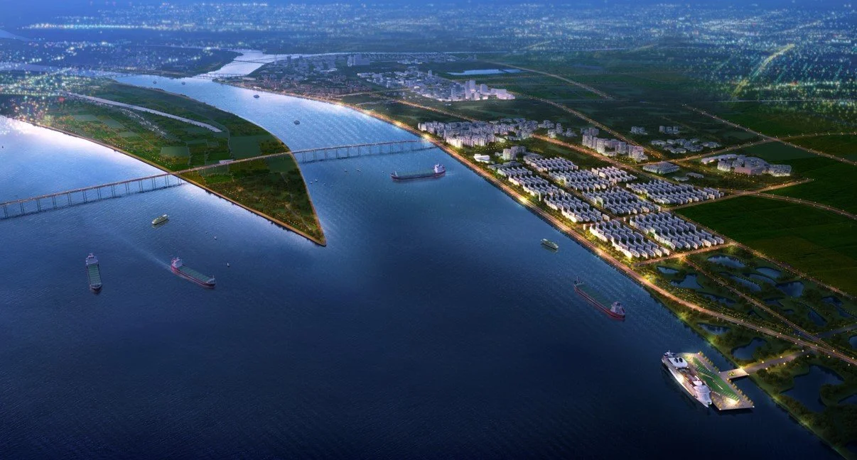 Aerial view of a city waterfront with several ships, bridges, and a mix of residential and industrial buildings at dusk.