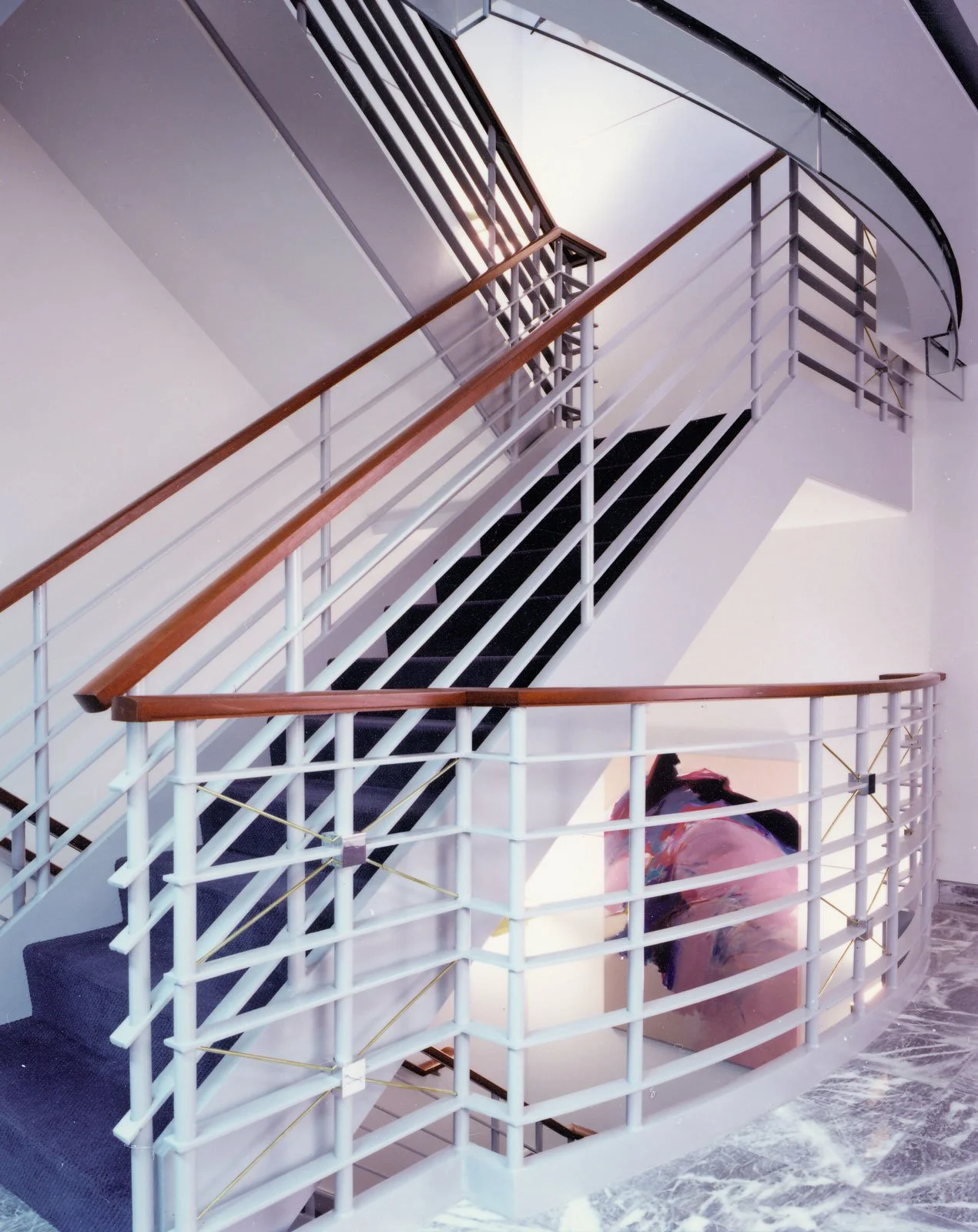 Modern indoor staircase with curved metal and wood railings, black steps, and marble flooring, viewed from below.