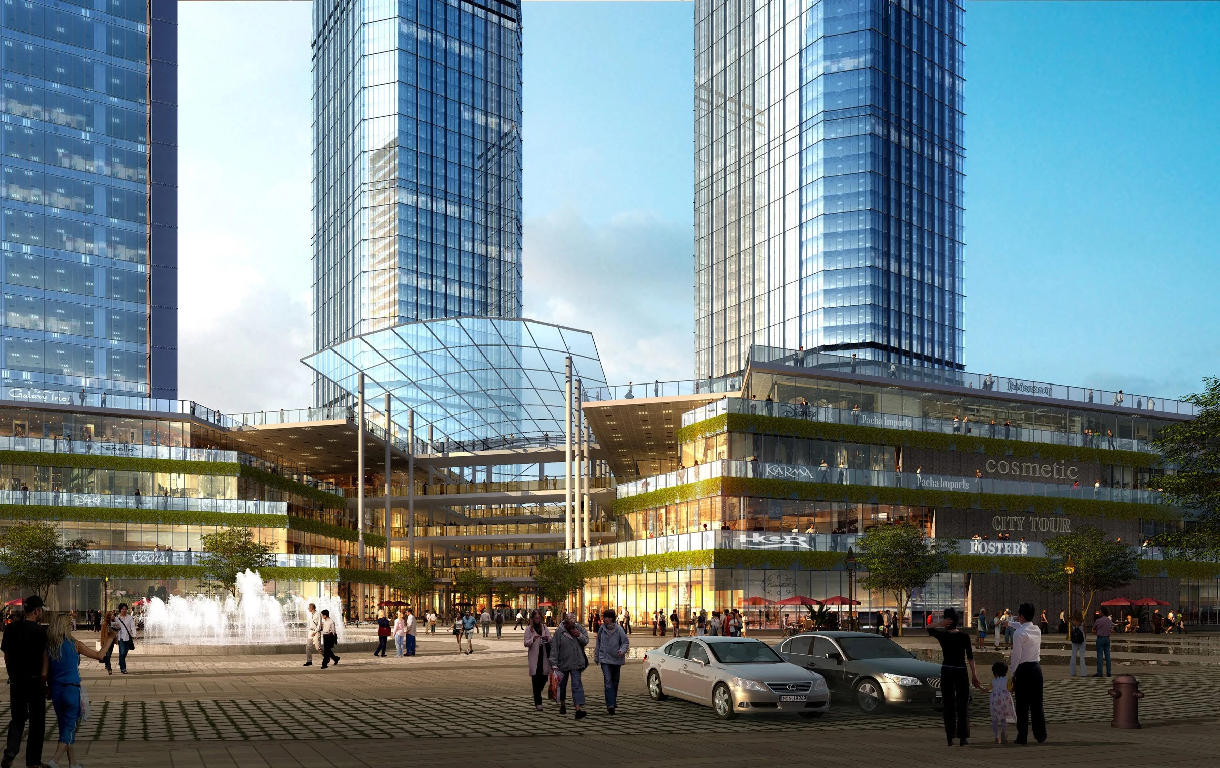 A city scene with tall glass skyscrapers and a multi-level shopping mall at the base. People are walking and standing outside, and cars are parked in front. There is a fountain and trees in the foreground.