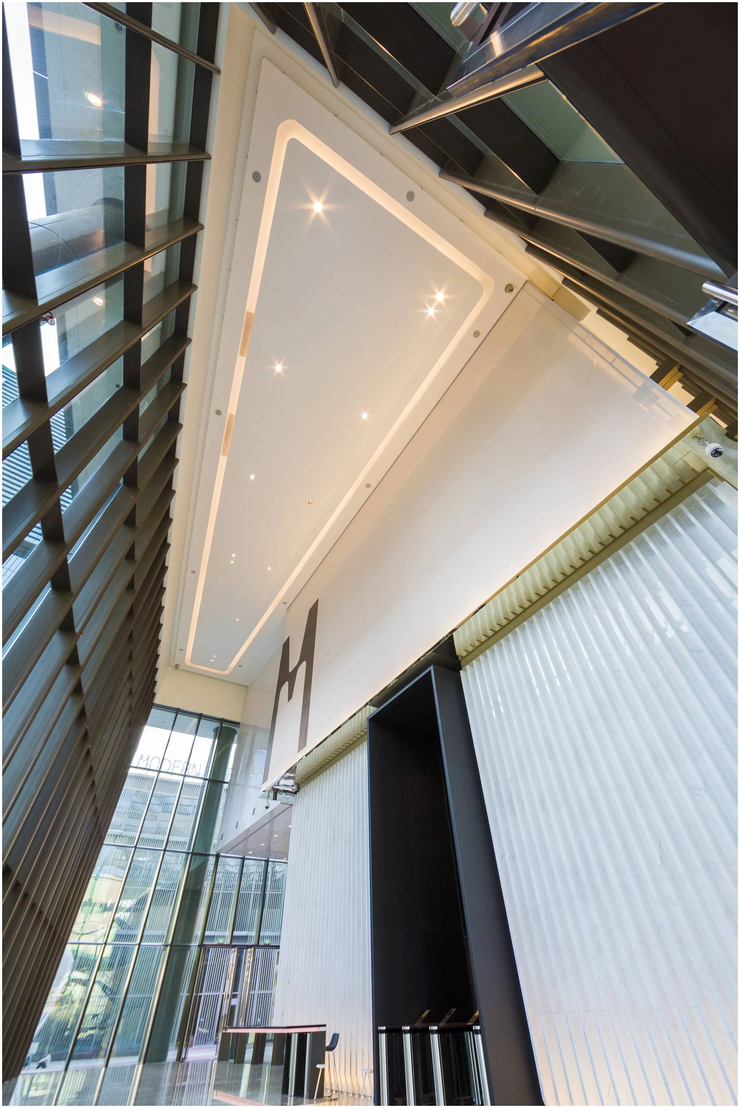 Modern interior of a building with tall glass windows, unique ceiling lighting, and sleek black and white decor.