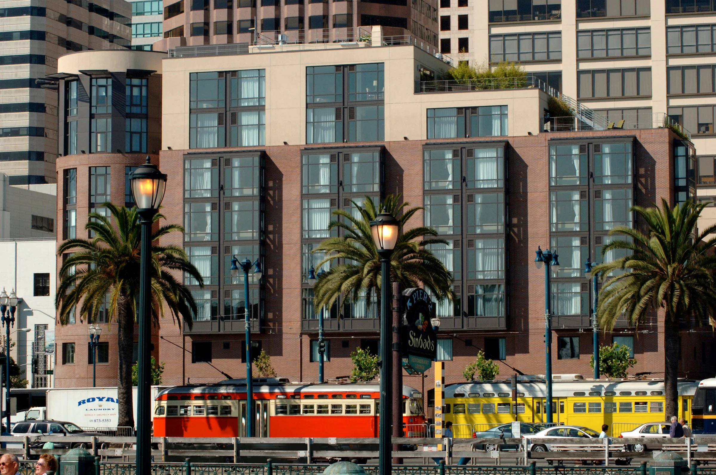 Street scene with palm trees, vintage yellow and red streetcars, and a modern multi-story building in San Francisco.