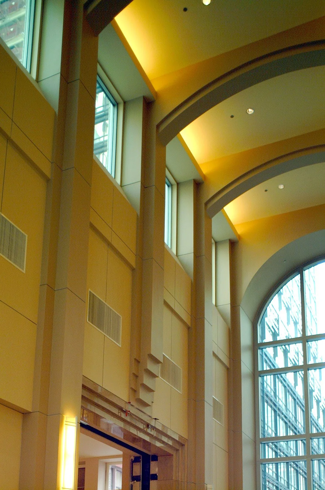 Interior of a modern building with a yellow ceiling, large arched and rectangular windows, and beige walls featuring vertical architectural details.