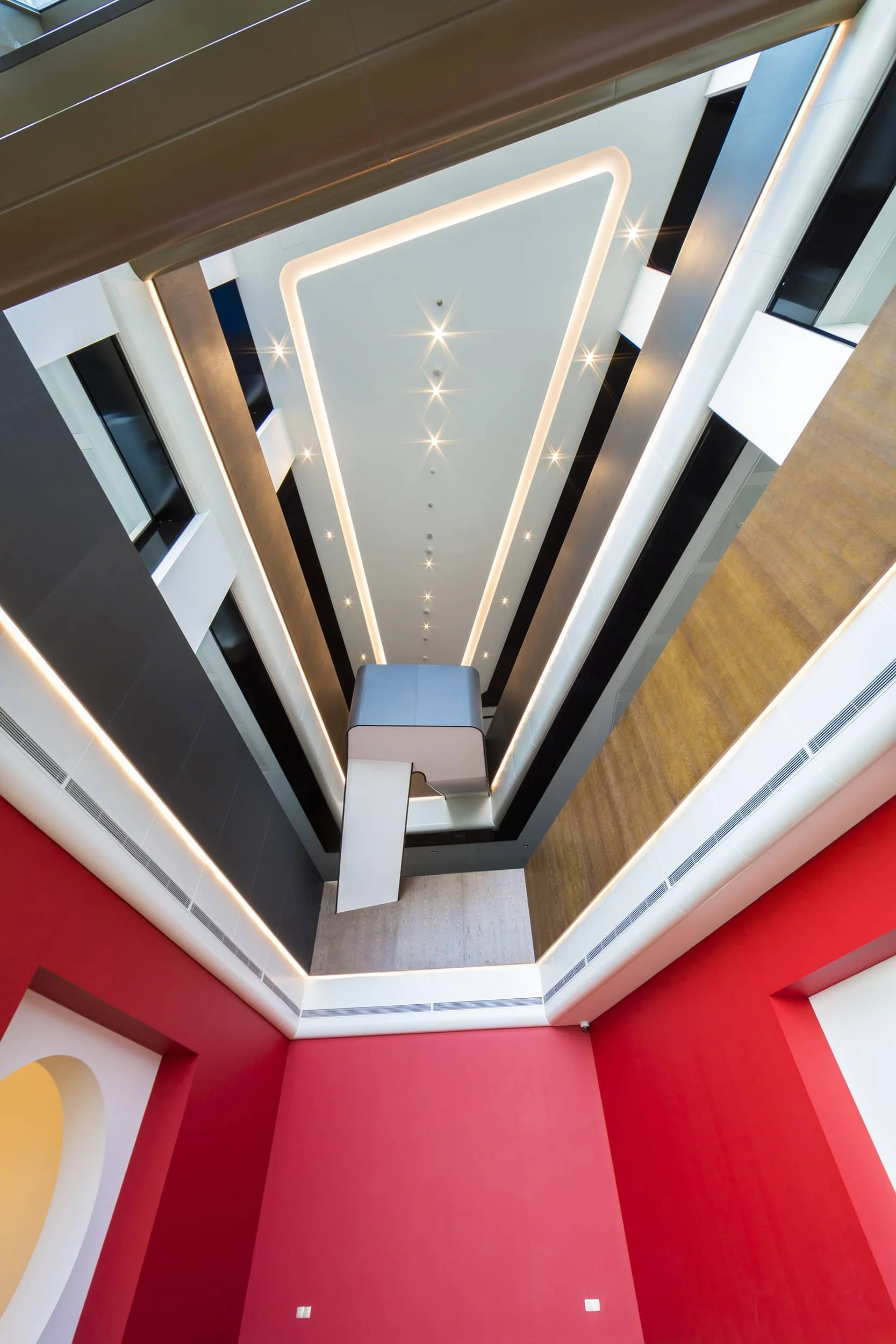 Looking up at the interior of a modern hotel or office building with multiple floors, featuring illuminated ceiling lights and geometric design elements.