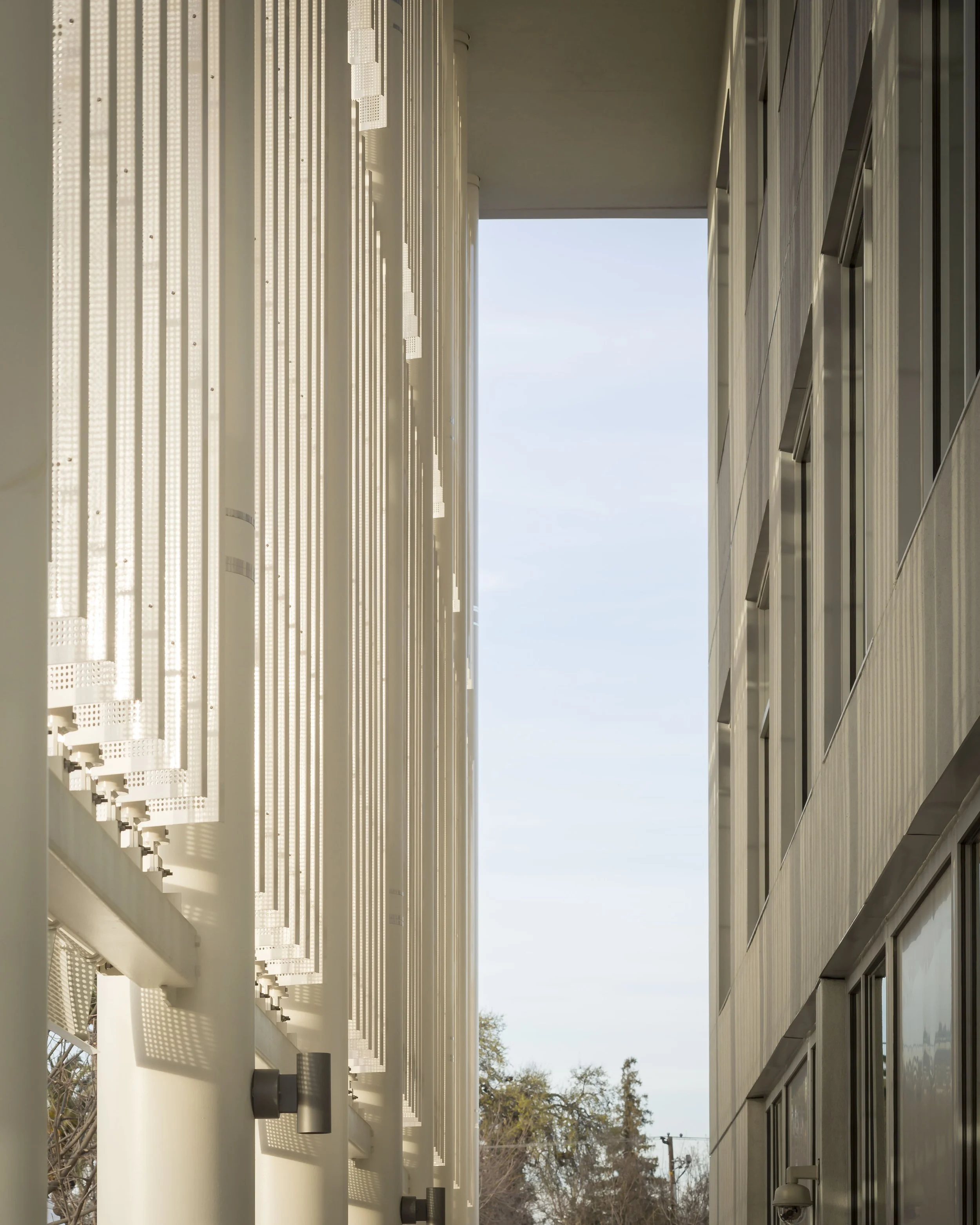 View between two modern buildings with blue sky and trees in the background.
