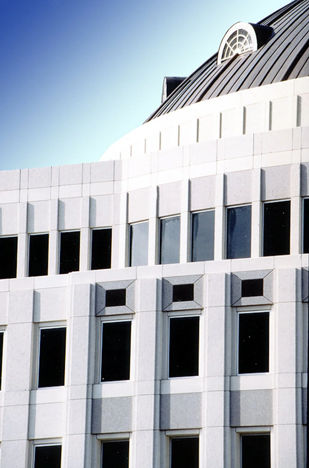 Close-up of a modern white building with large windows and distinctive architectural details, including vents and a rounded roof with skylights, against a clear blue sky.