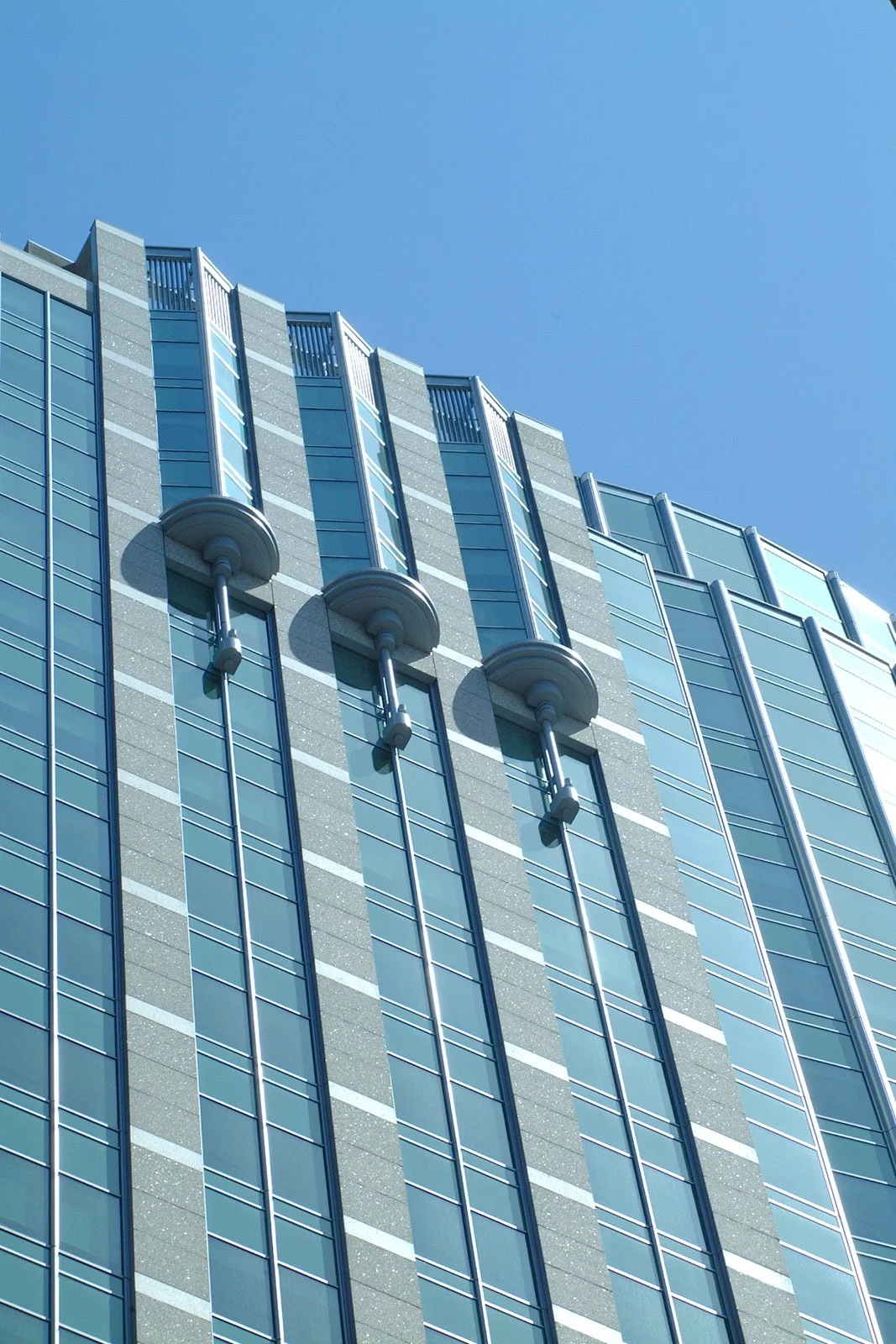 Close-up of modern glass and concrete skyscraper with vertical grid pattern and circular architectural features against a clear blue sky.